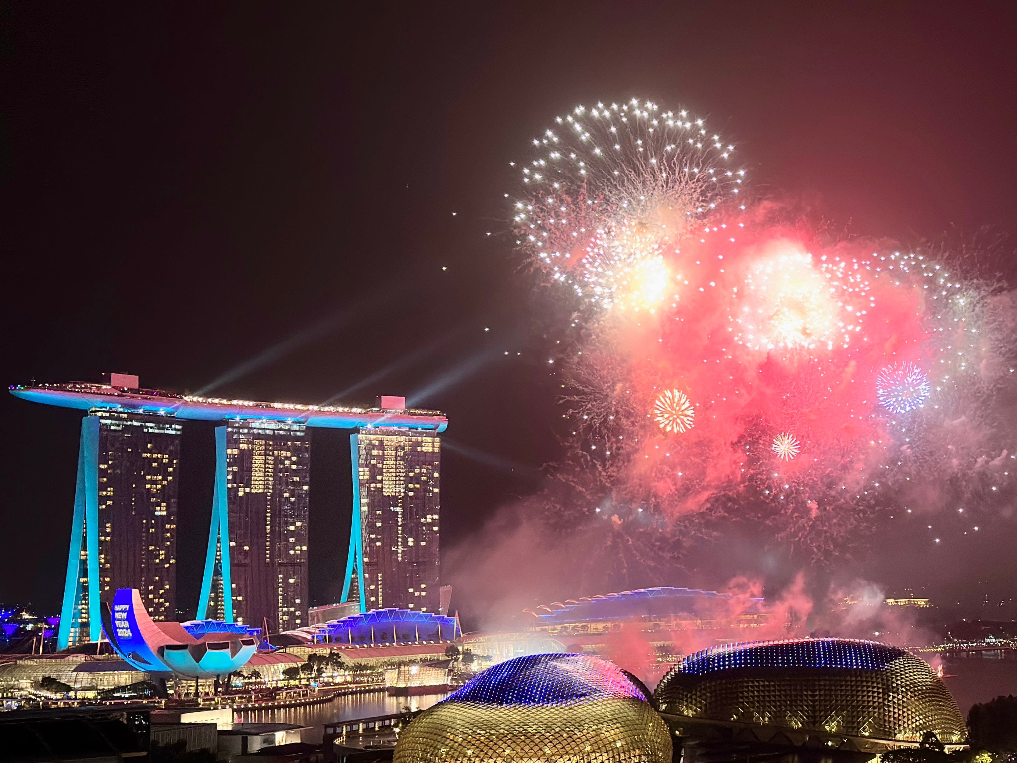 A view of a colorful firework display and illuminated tall skyscrapers at night