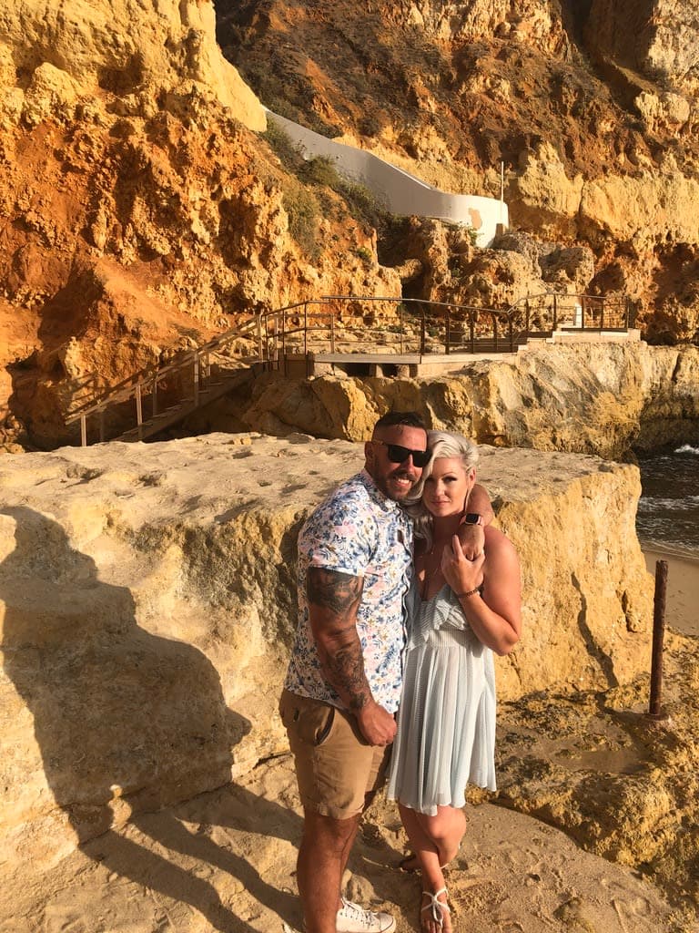 Brian and a woman in tropical attire posing in front of rock formations