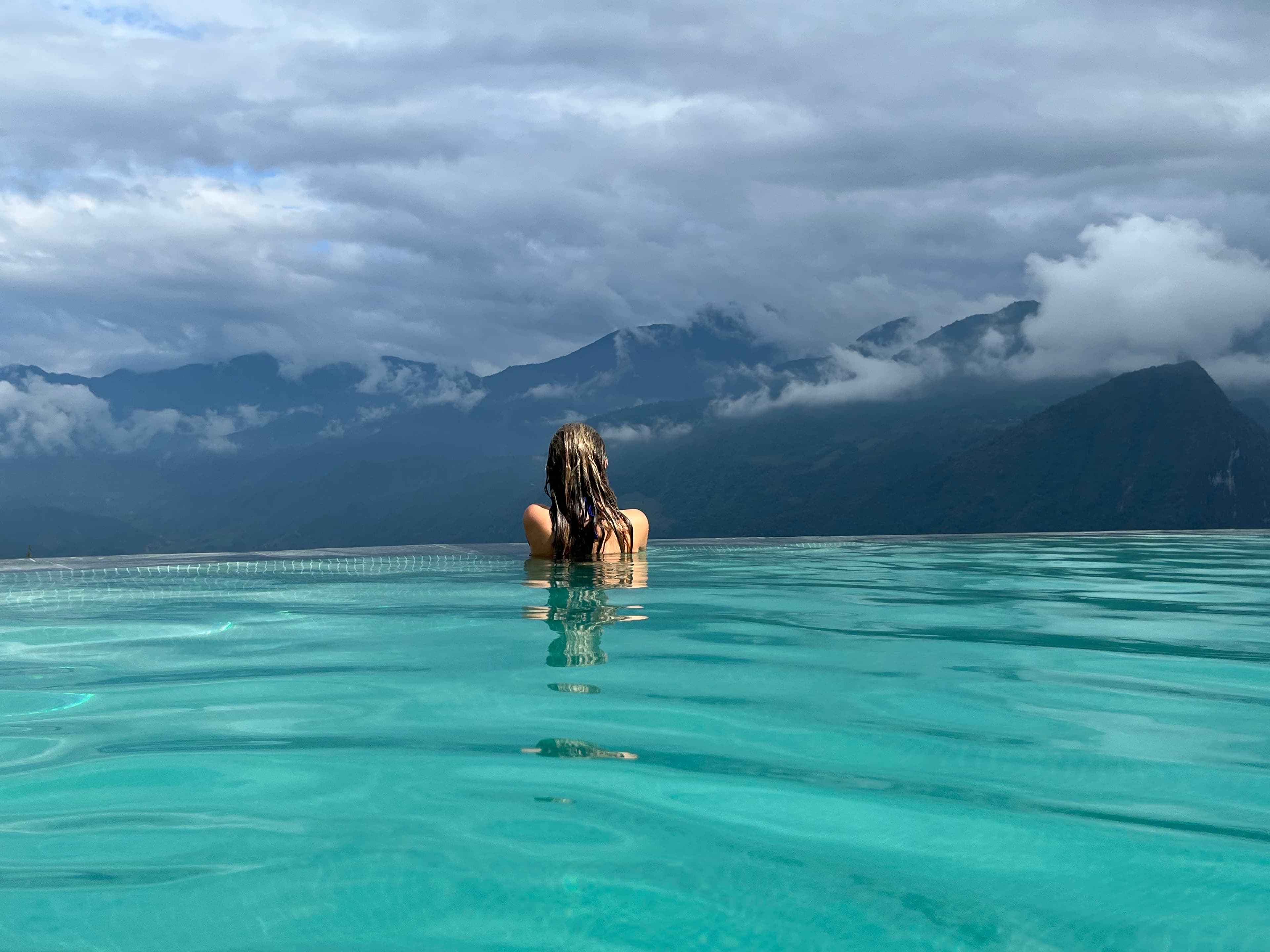 Rear view of woman in infinity pool overlooking mountains with clouds
