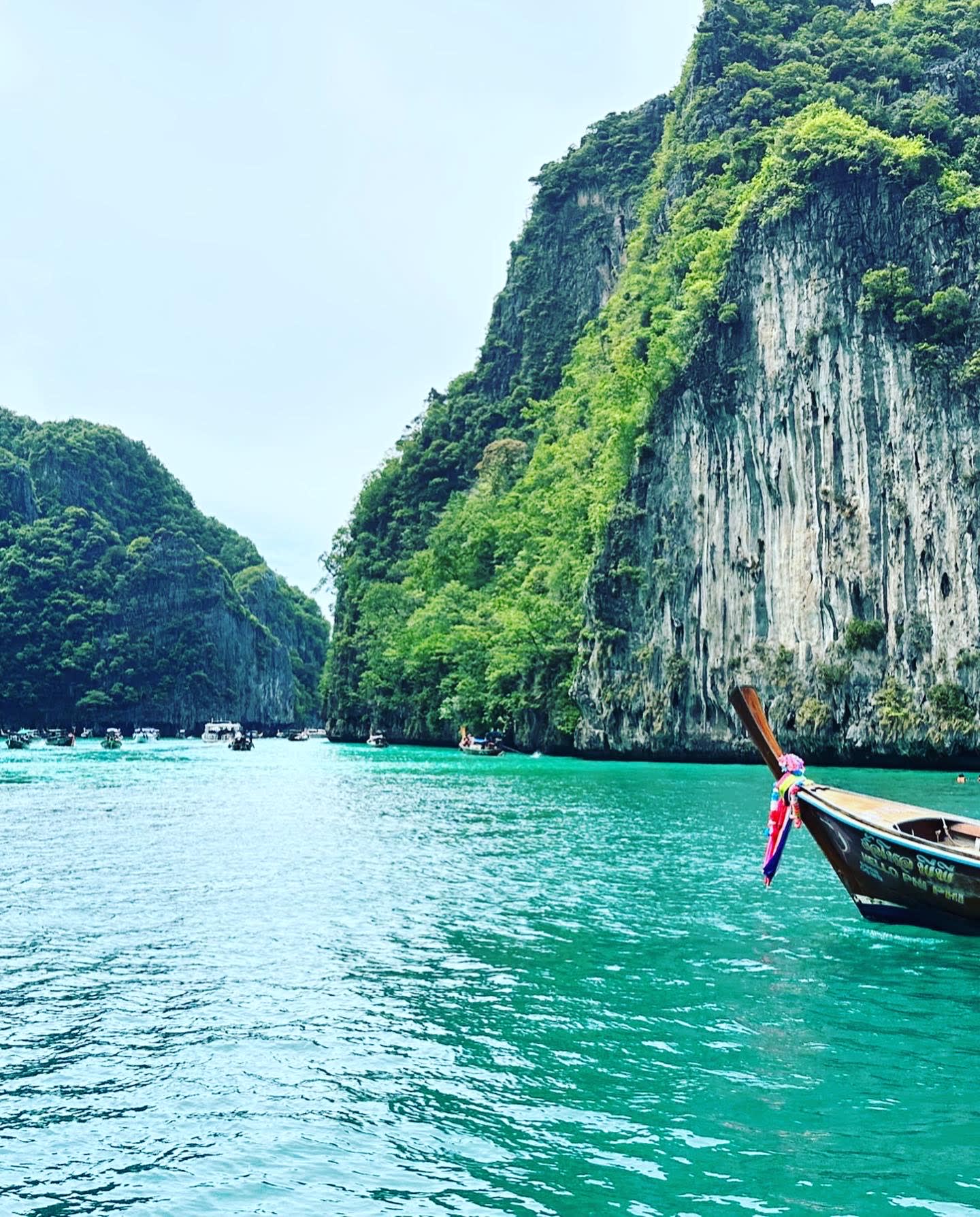 Turquoise colored water with cliffs ahead with green foliage and a small boat in view