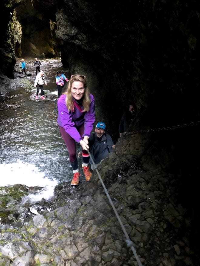 Anne in a purple jacket climbing a rock formation using a rope above a river