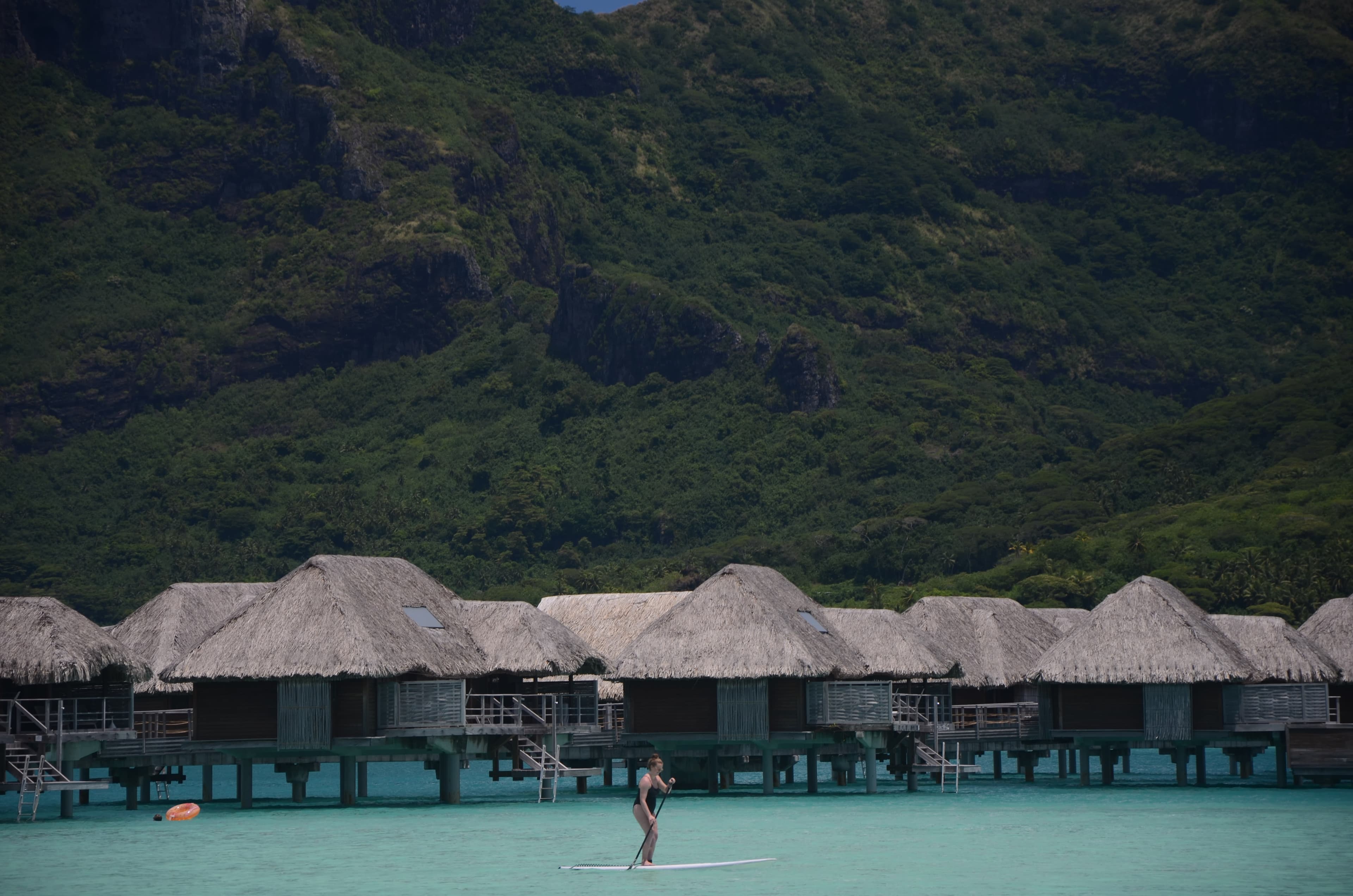 Gloria on a paddleboard in front of overwater huts in front of a large green hillside