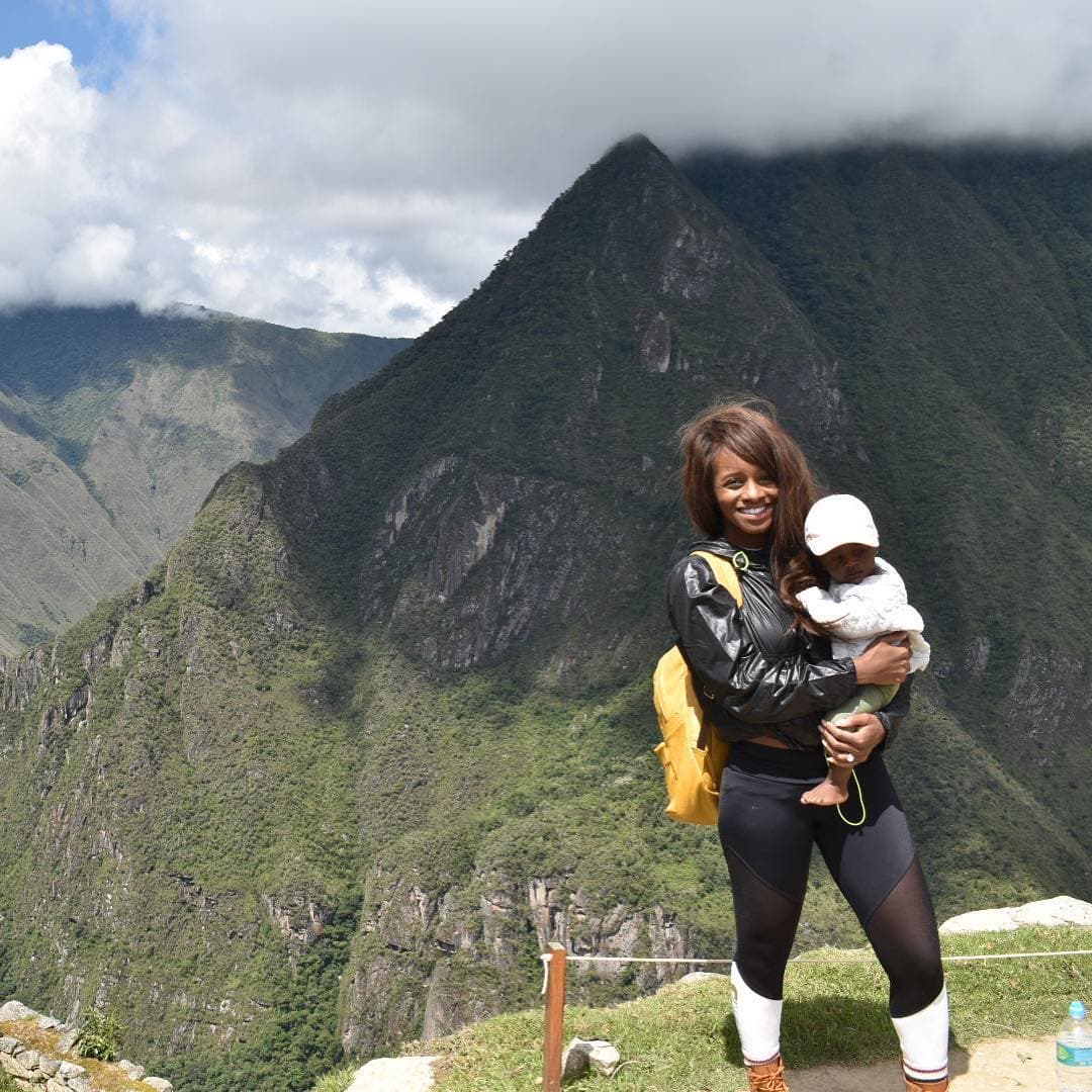 Sitaara holding a baby on a trail with mountains in the background
