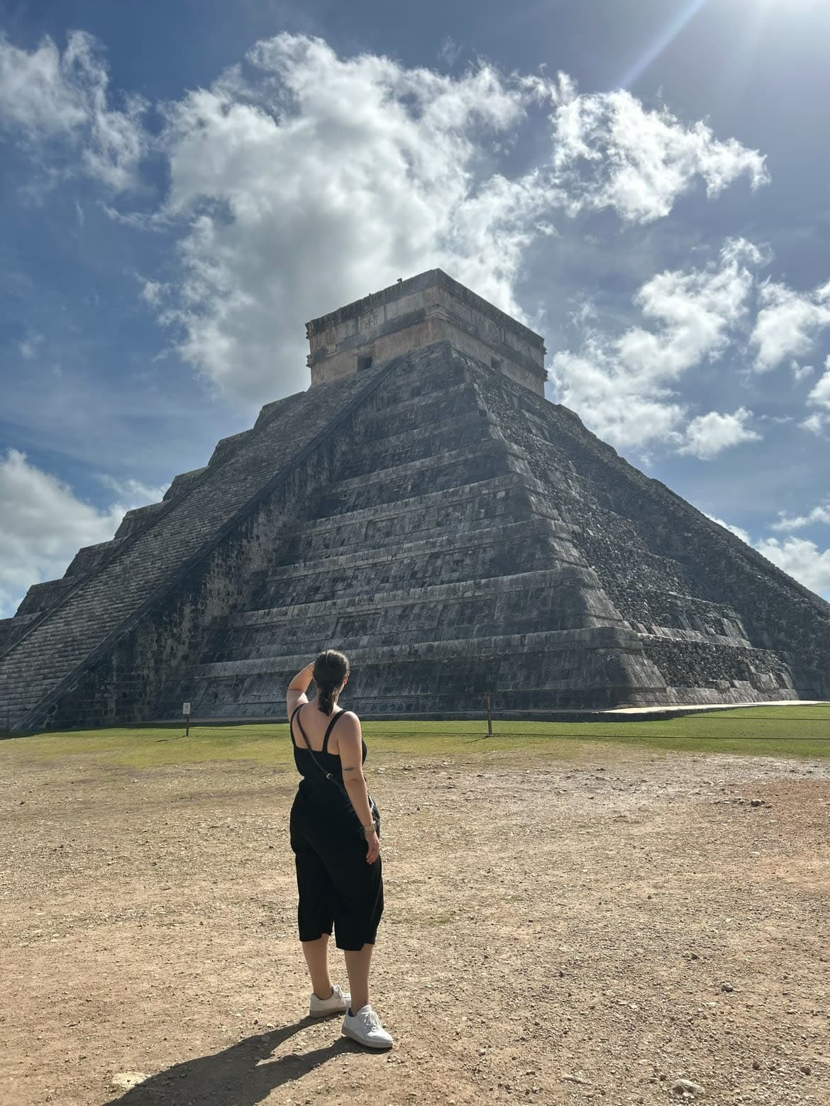 Savannah in a black jumpsuit and sneakers looking at a stone pyramid.