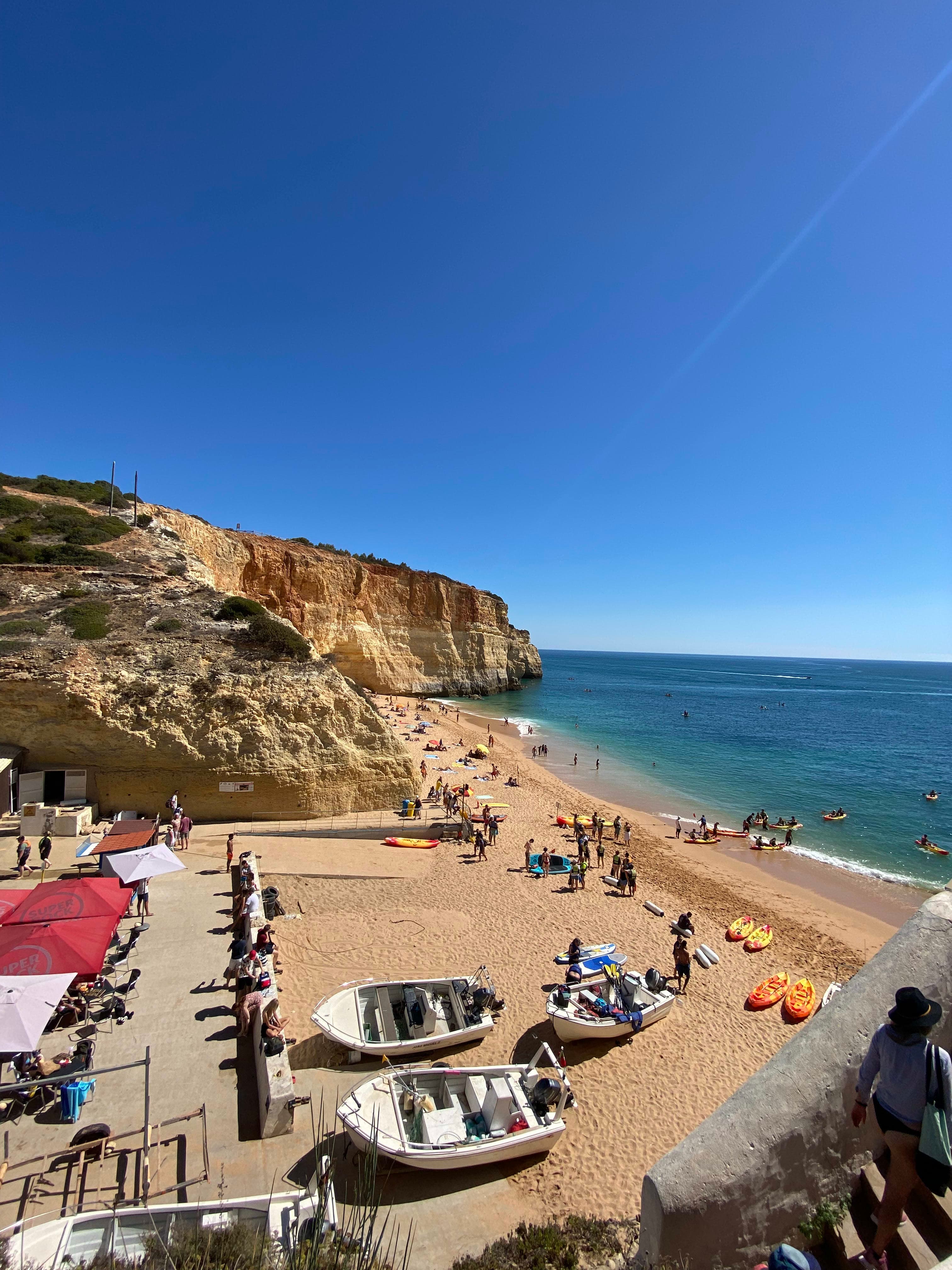 Boats and umbrellas on a beach next to rocky cliffs.