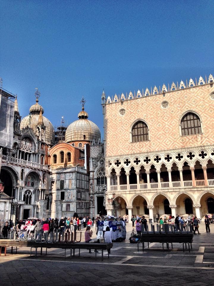 A city square with domed buildings and Middle Eastern architecture and tourists sitting on benches.