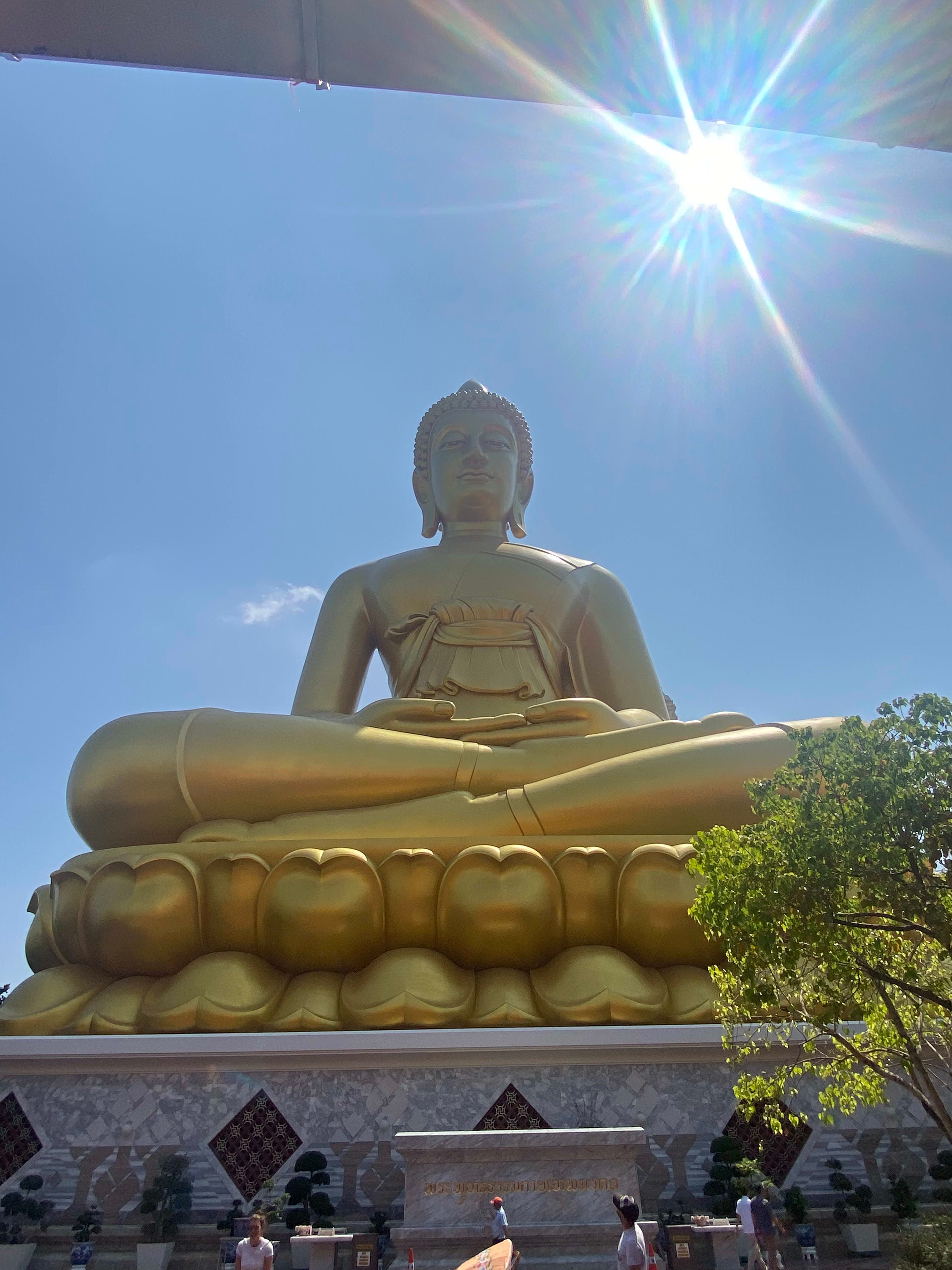 View of Paknam Phasi Charoen Temple from below the giant statue of a golden buddha sitting cross-legged.