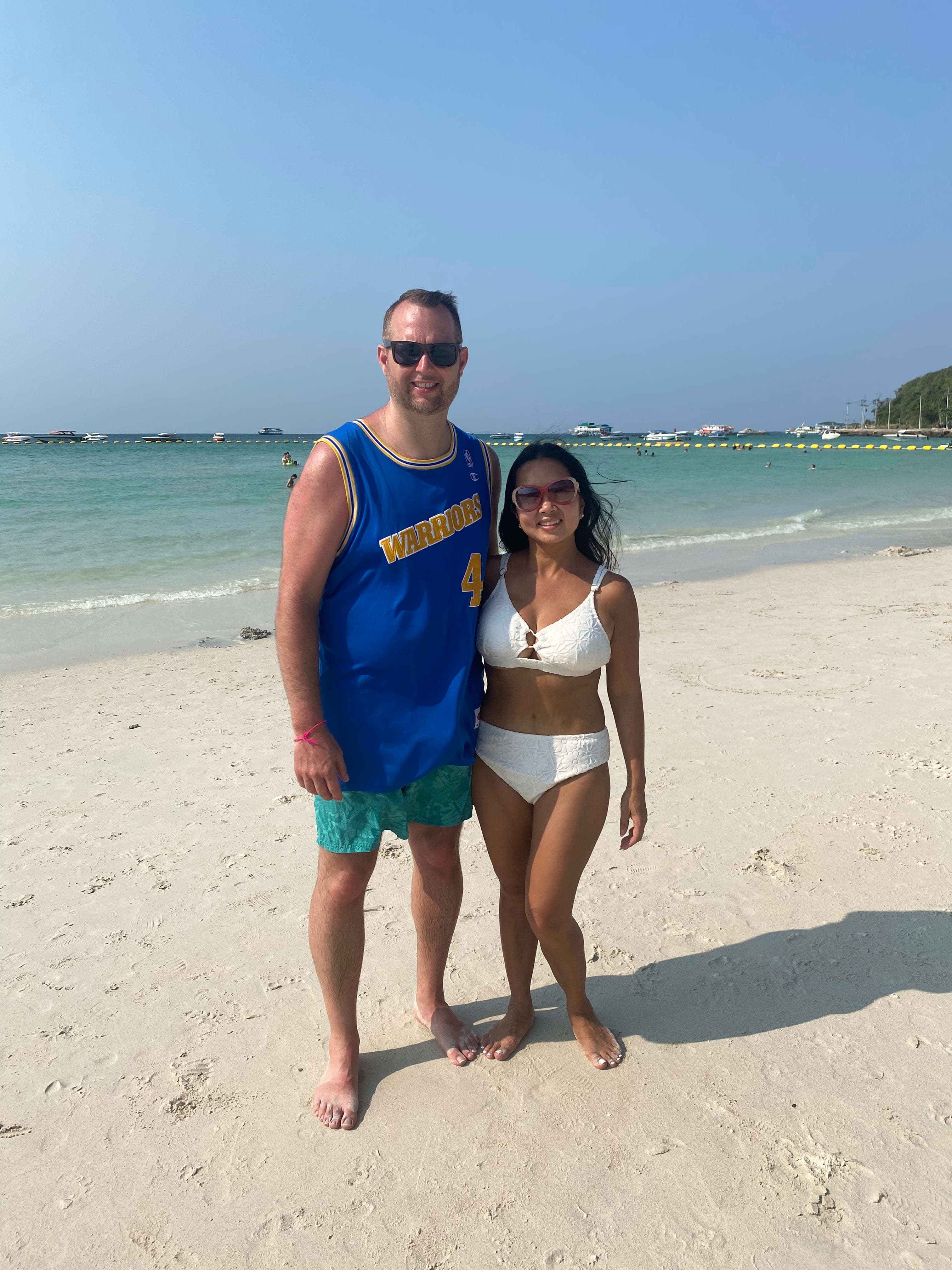 Picture of Anne and a man standing on the beach in bathing suits with clear blue shoreline in the background