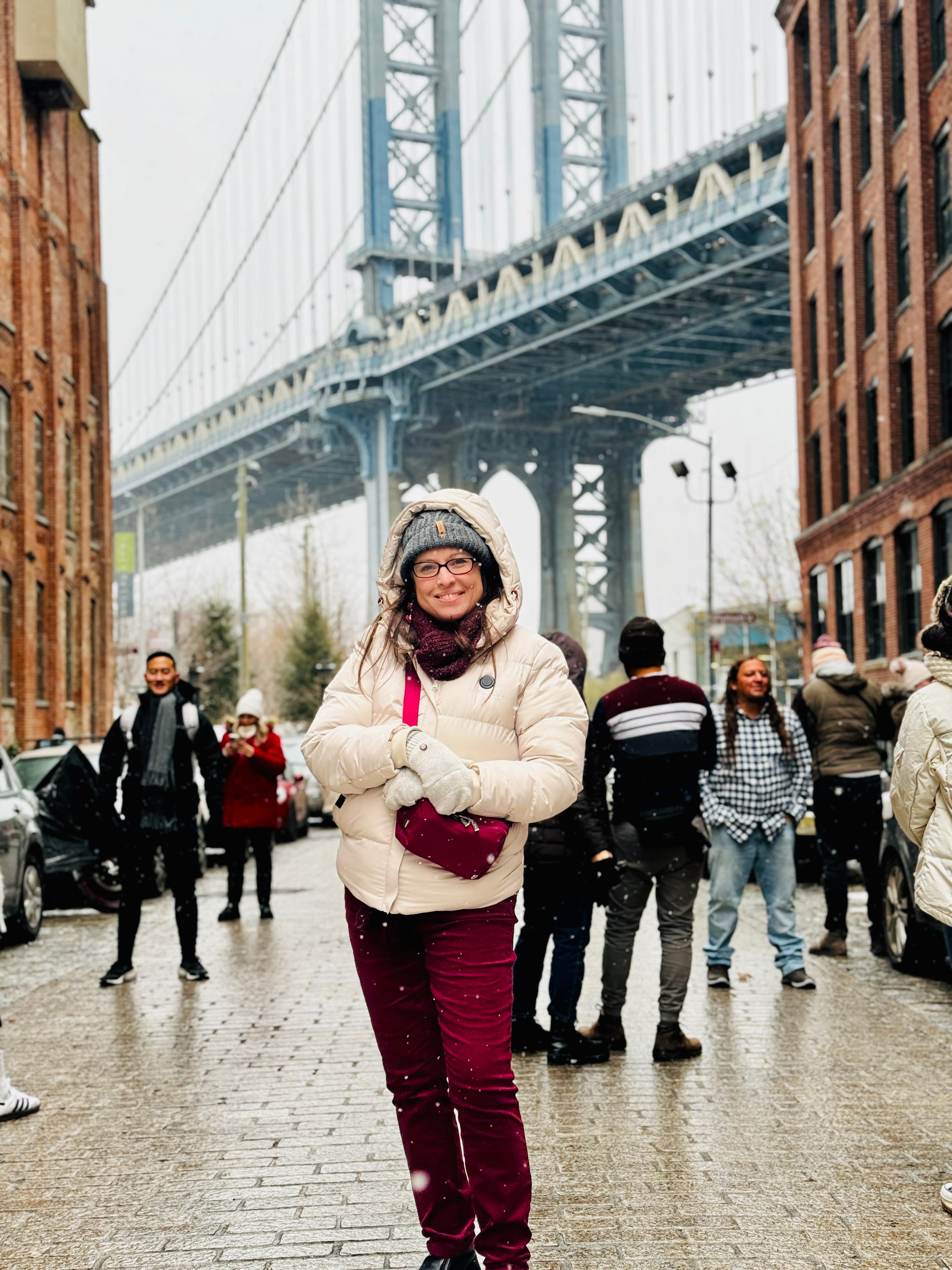 Lauraliisa wearing winter clothes and posing for a photo on the street with the Brooklyn Bridge in the background.