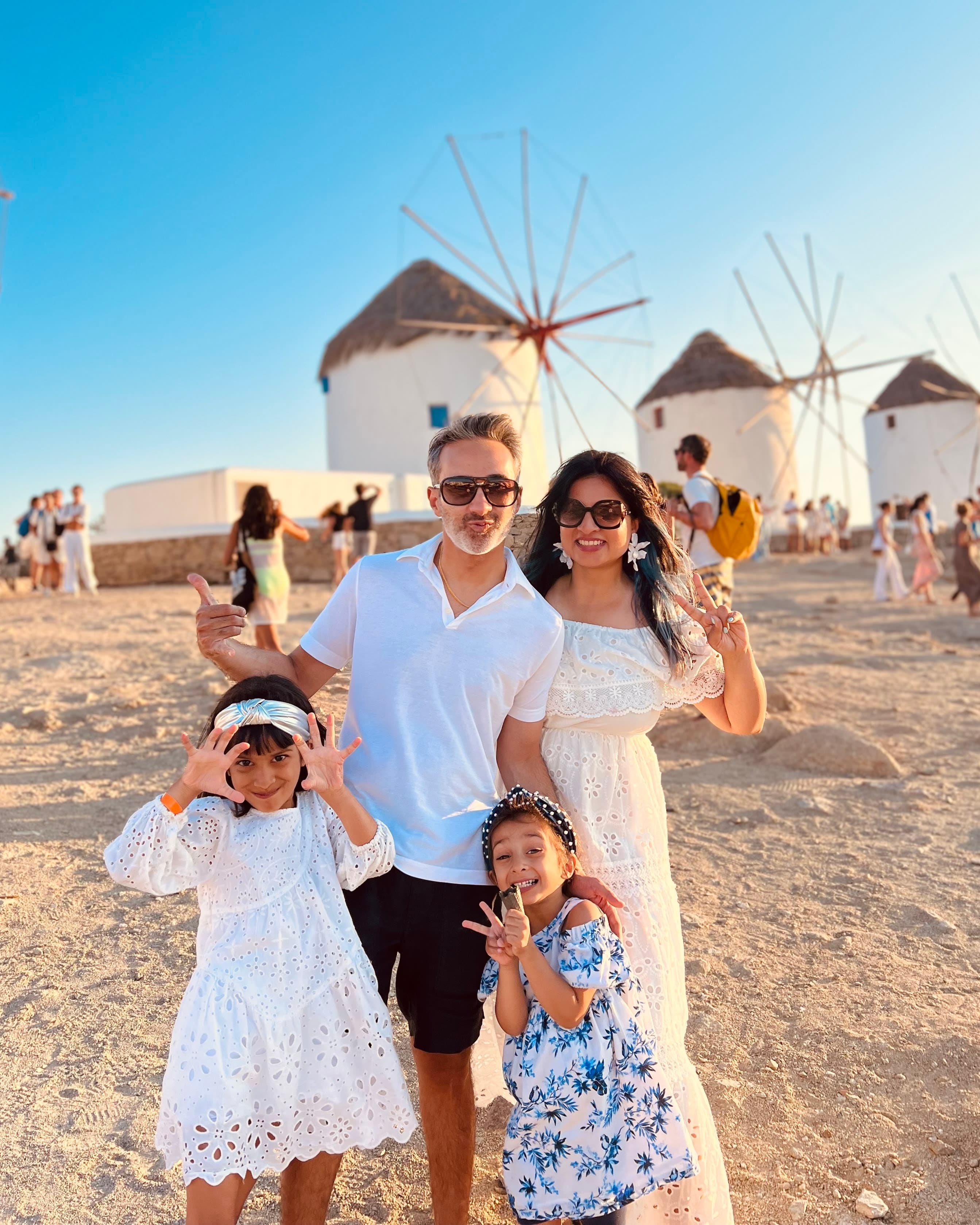 Travel advisor Kavita Shah posing with her family on sandy terrain in front of round white buildings with windmills on a sunny day