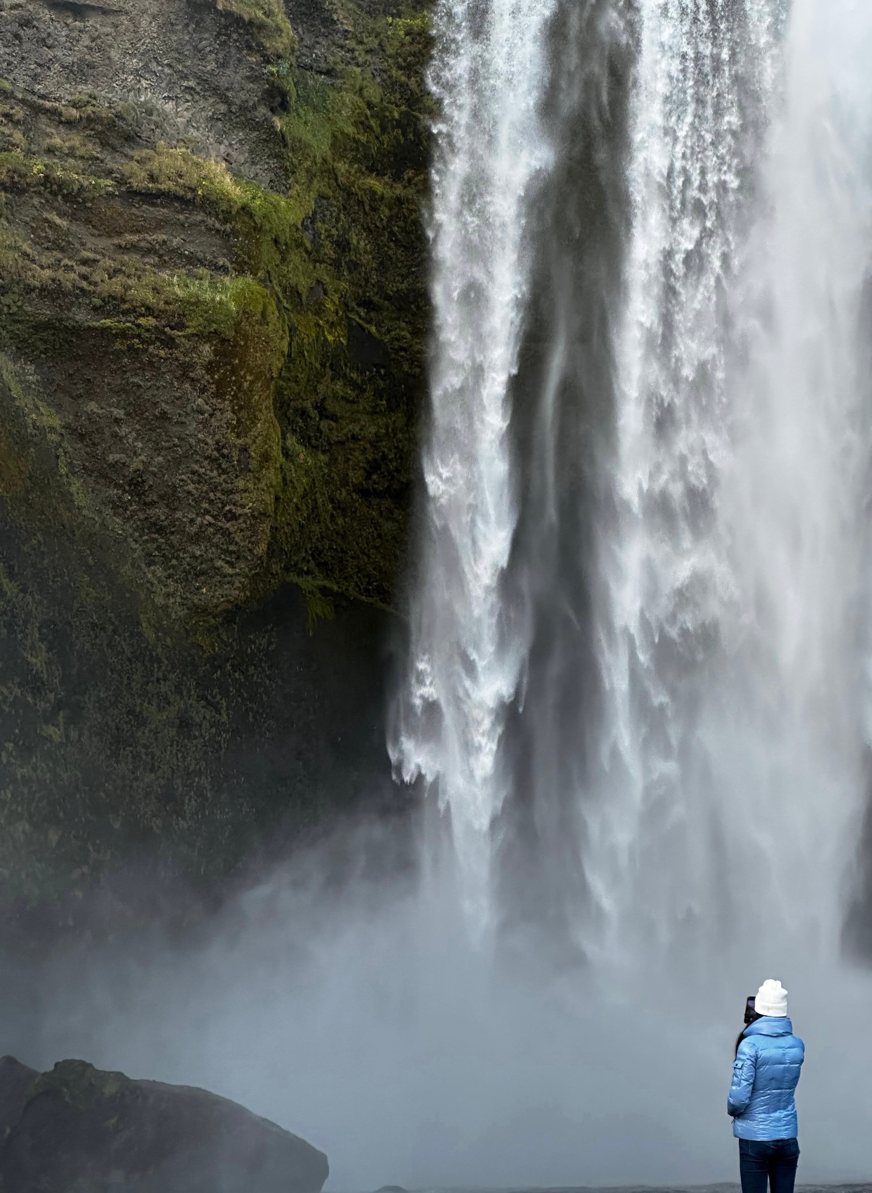 A picture of a person from behind admiring a large waterfall