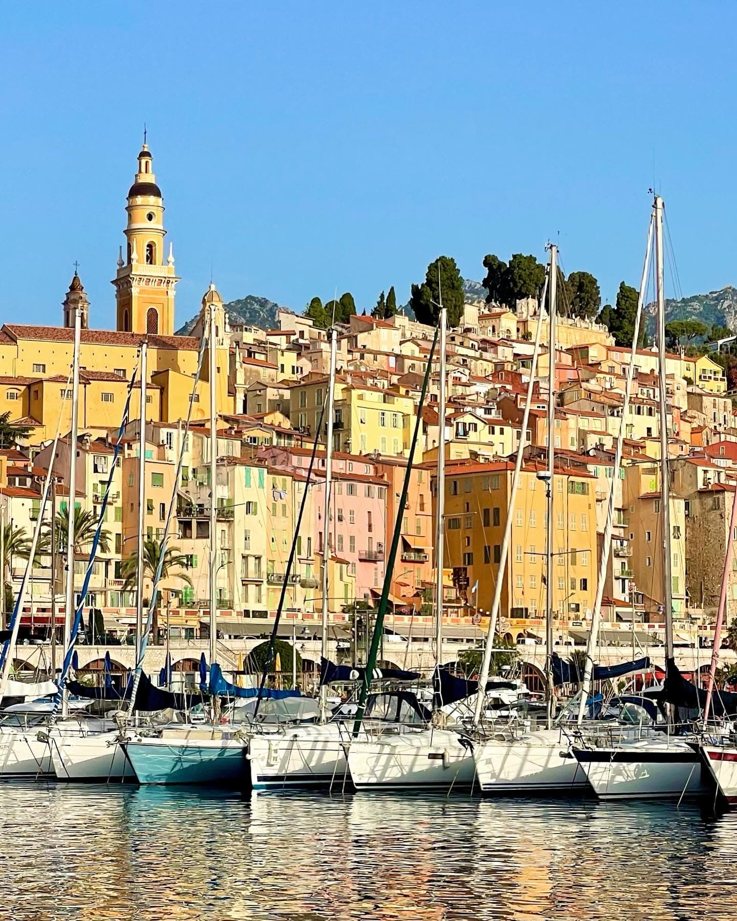 View of boats docked at a pier in front of a hillside full of pastel colored buildings