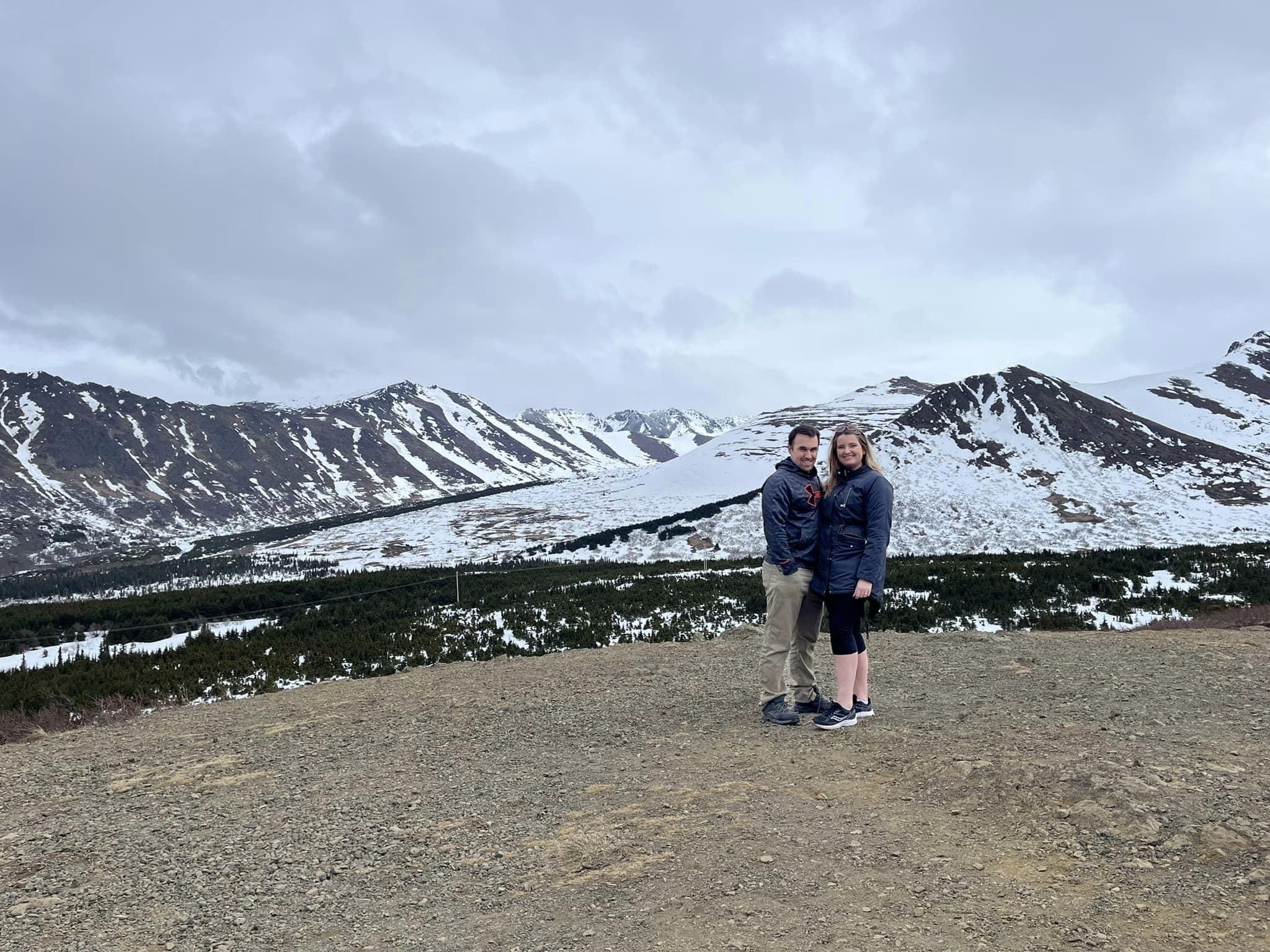 Leah and a man wearing jackets with snow covered mountains in the background.