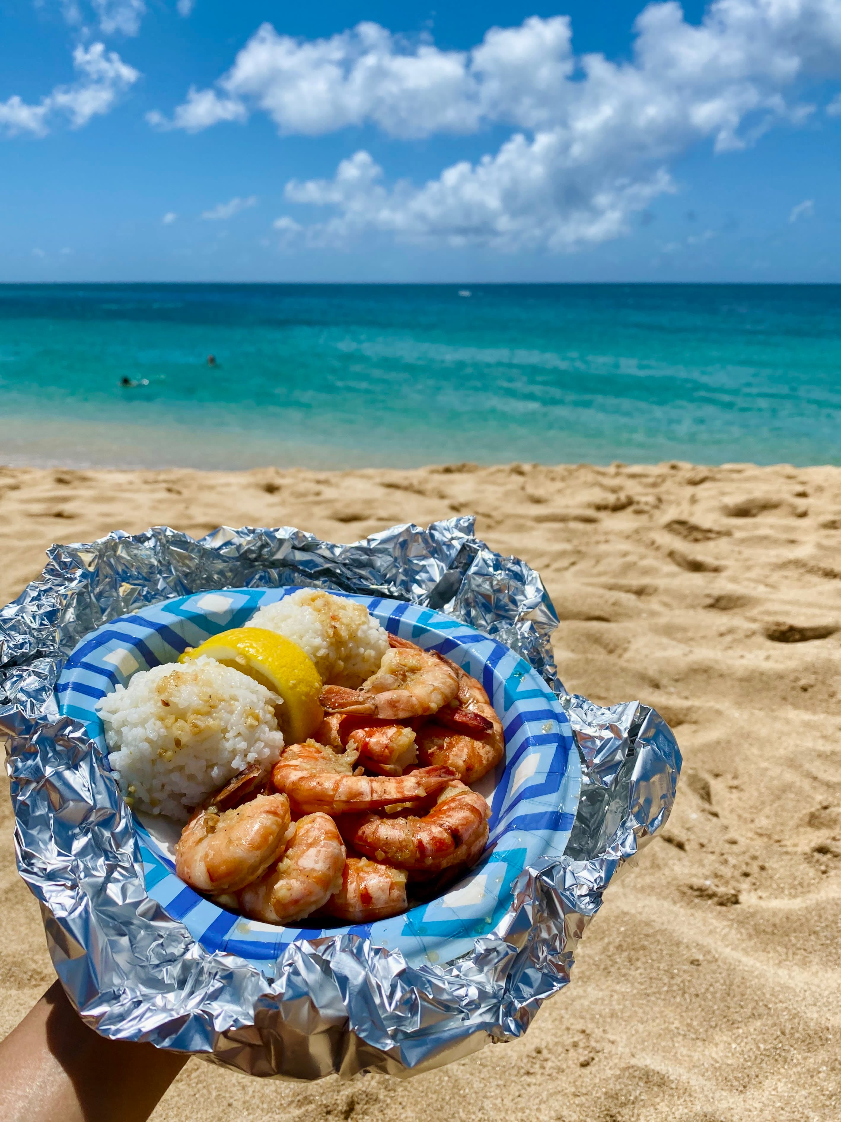Michelle holding up a paper plate filled with prawns on the beach