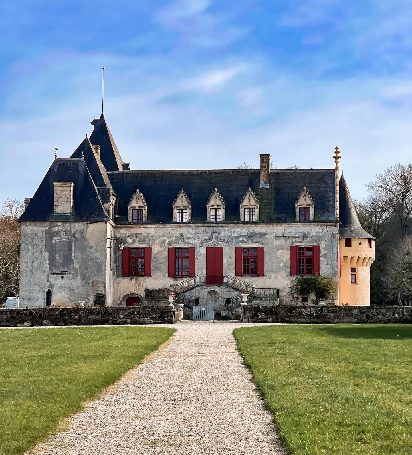 Path leading to Château Olivier, a stone house with red shingles and a black roof