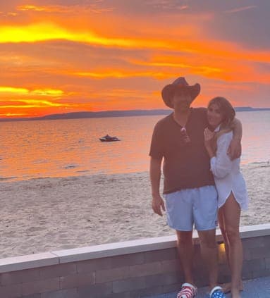 A man in a cowboy hat and a woman in a white dress posing in front of the ocean at sunset