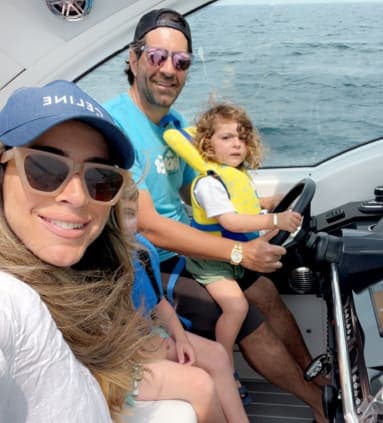 A woman in a cap and sunglasses, man in a cap and sunglasses and a child in a life vest posing on a boat