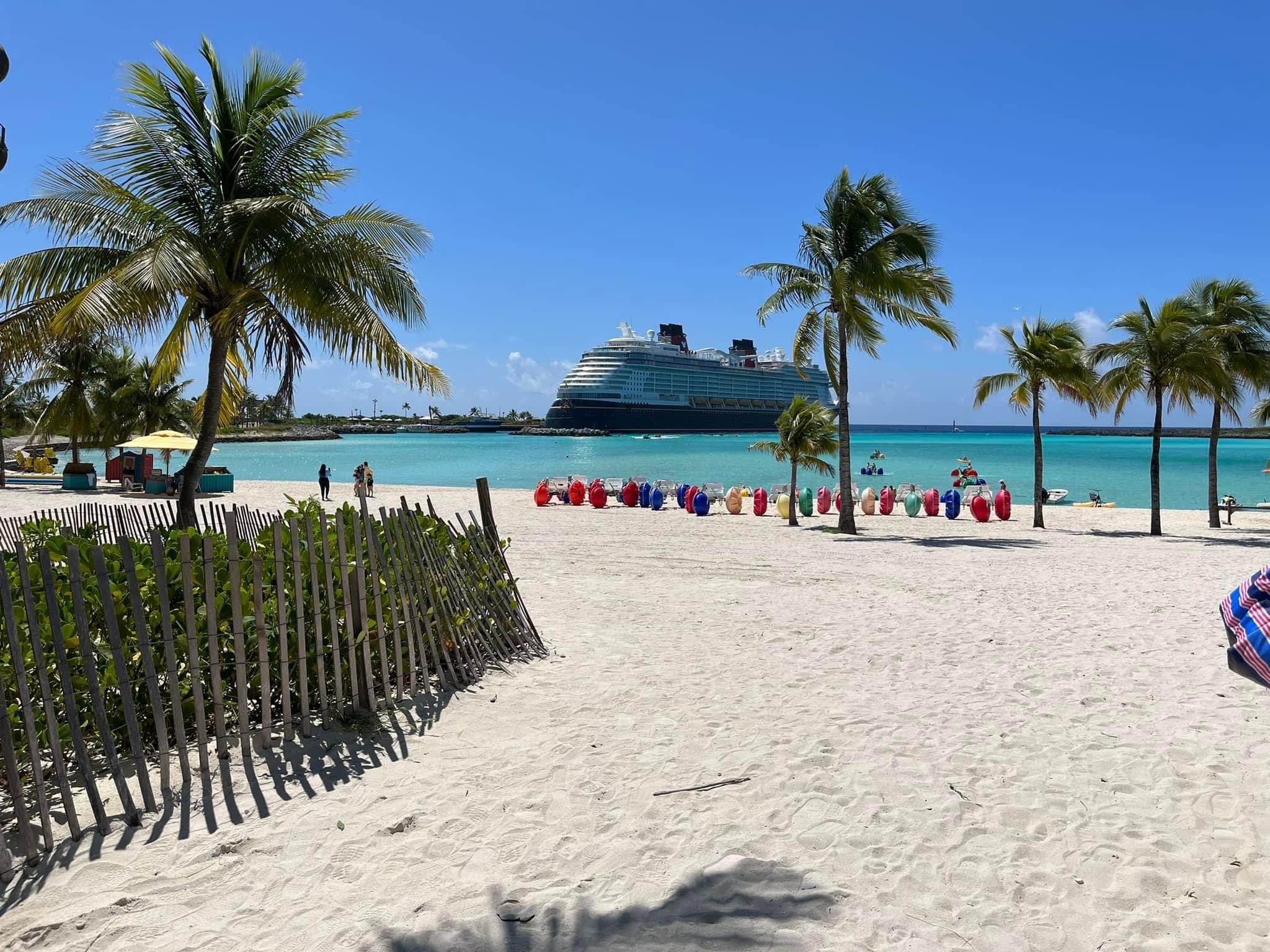A view of a beach with turquoise colored water and palm treets, and a cruise ship in view