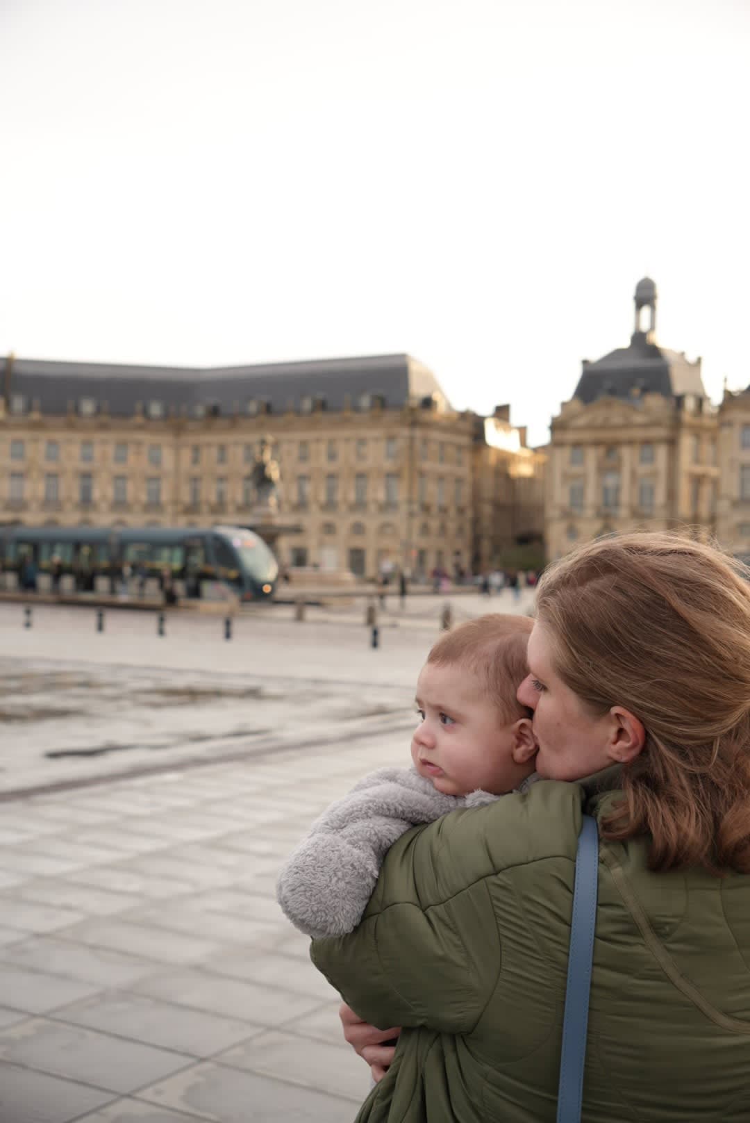 Alyssa standing in front of the Bordeaux Place holding her baby in the arms