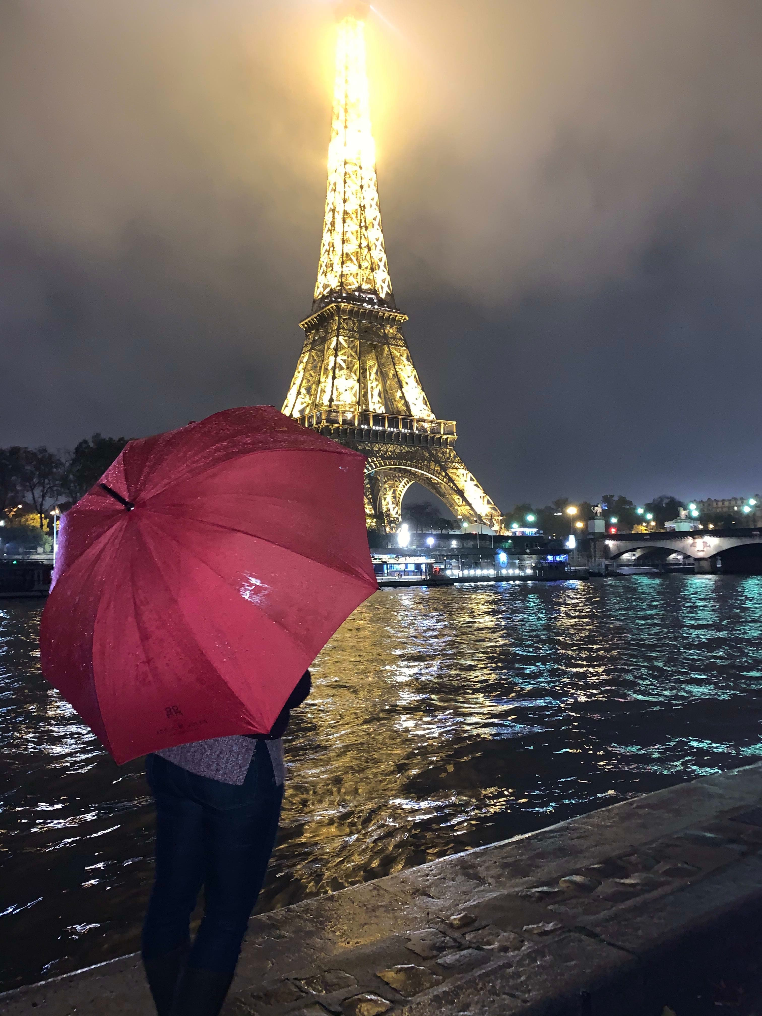 A person holding a red umbrella looking at the view of the Eiffel Tower lit up at night