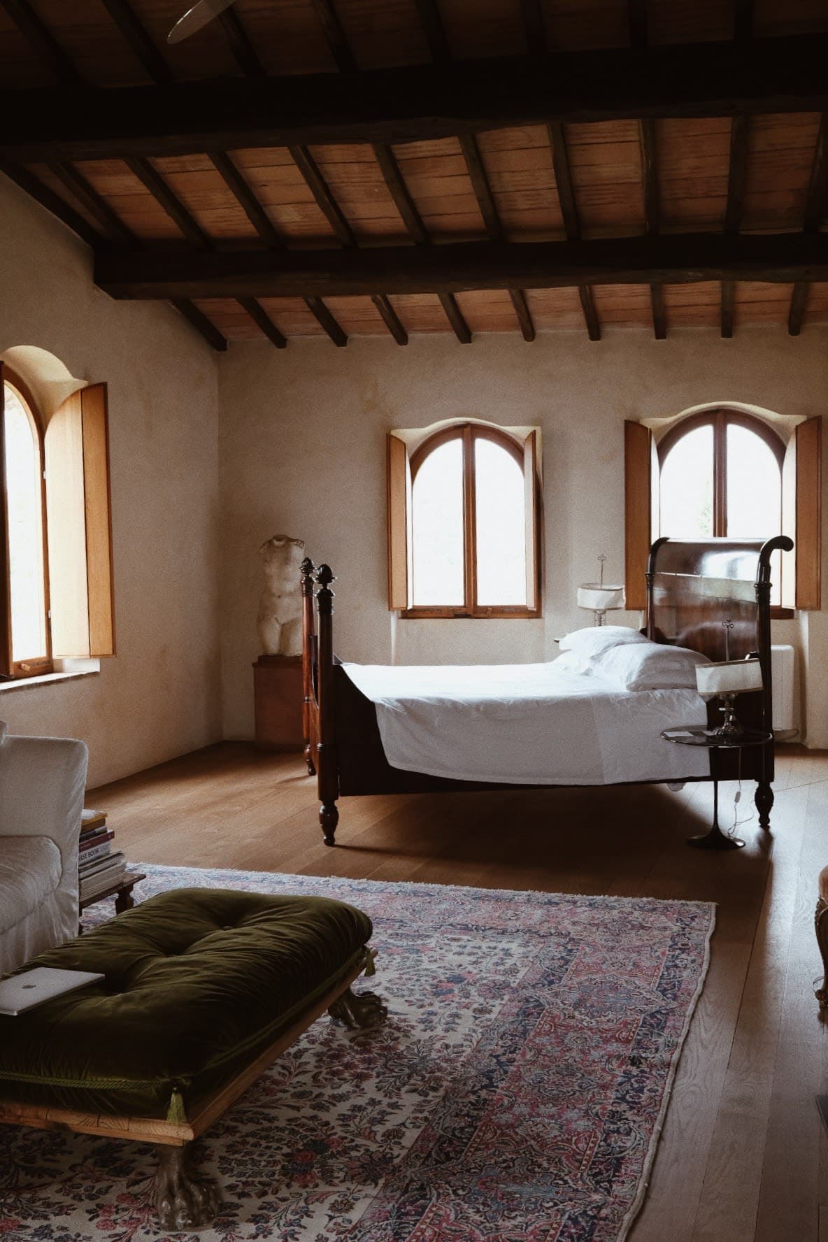 View of a room with bed in focus, wooden slat ceiling and a sitting area on the side