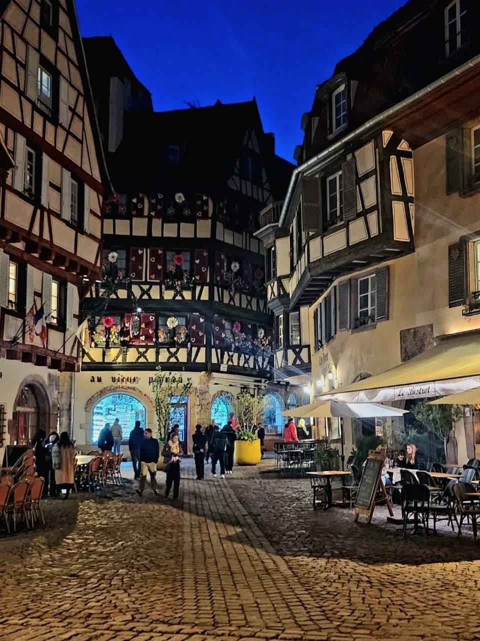 View of Colmar, France at night with Tudor-style quaint buildings and cobblestone streets.