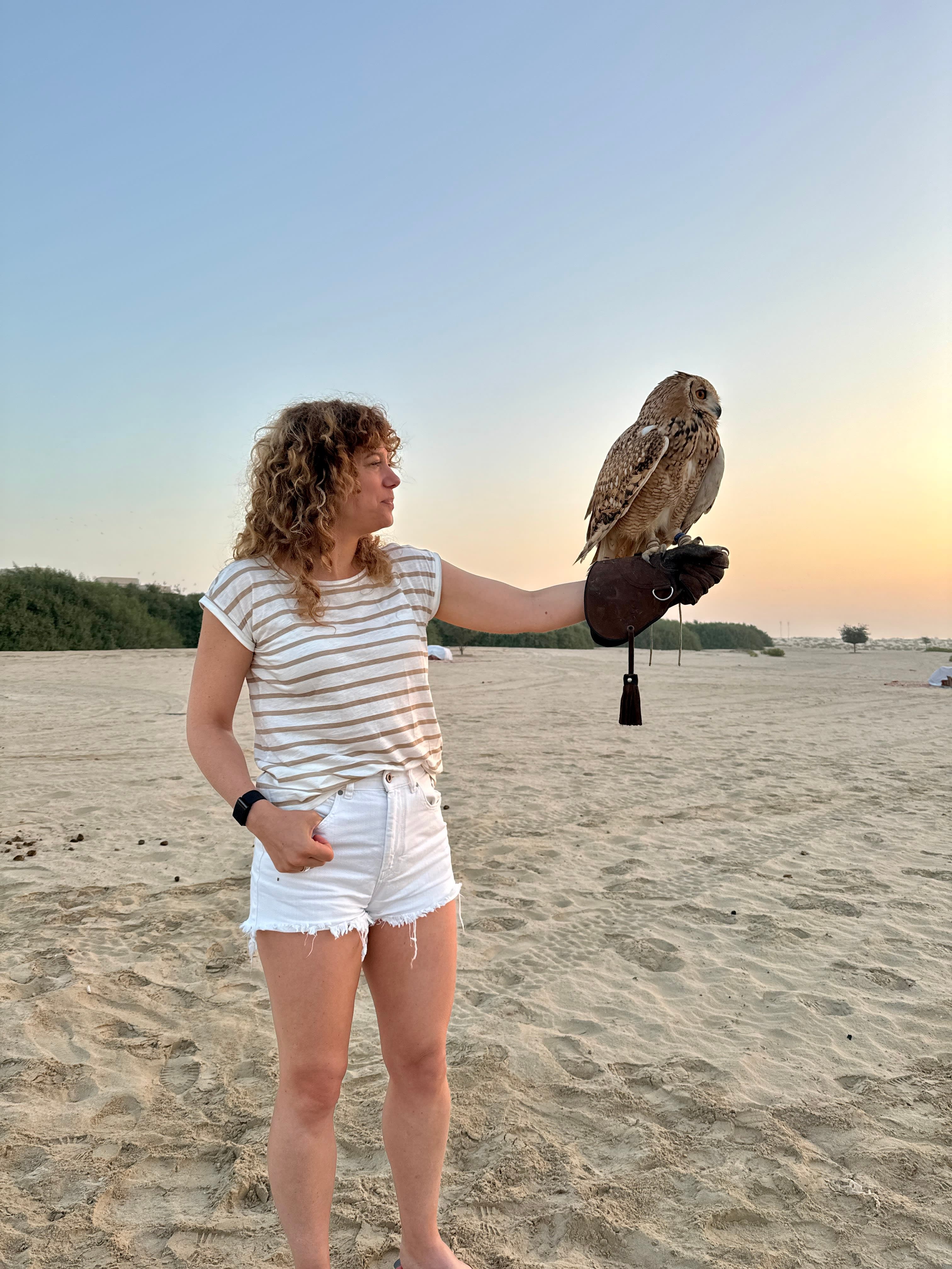 Travel advisor Alexandra standing on the sand at sunset holding an owl
