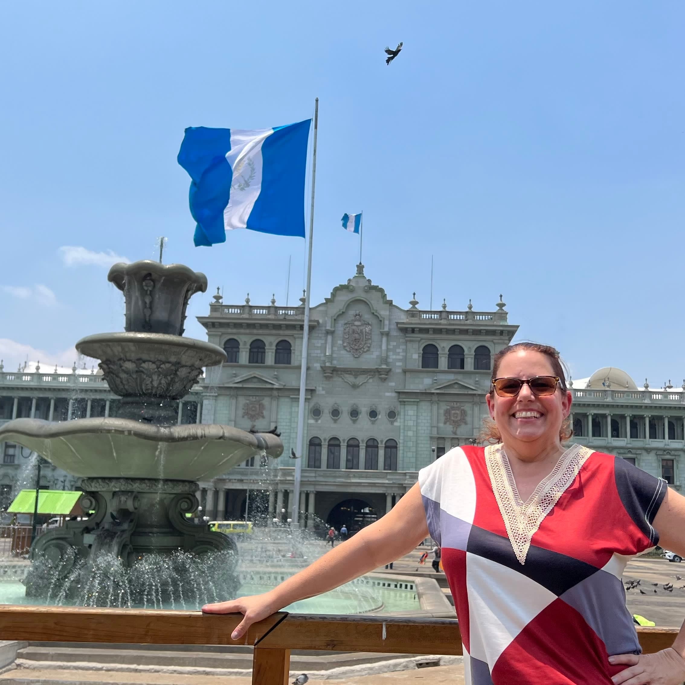 Vivian posing for a photo in front of the National Palace of Culture, a classical building with a blue and white flag in front