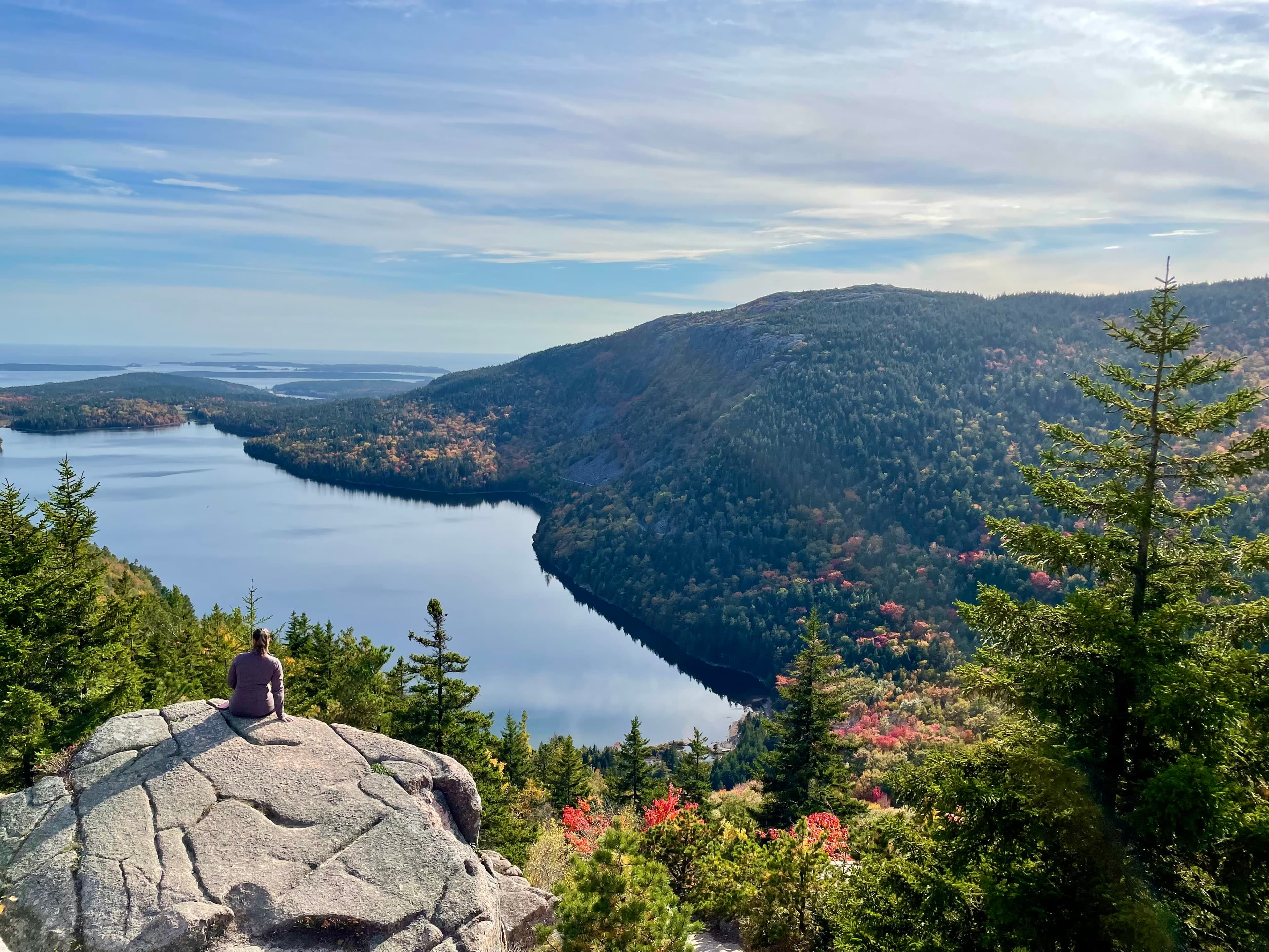 Elizabeth sitting on a large rock overlooking a lake with tree-covered hills surrounding it.