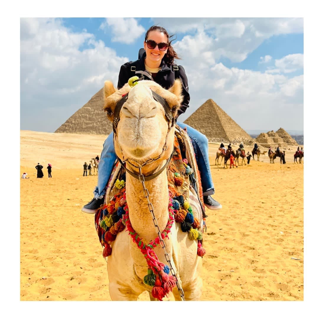 Britnee sitting on a camel in the desert with pyramids in the background