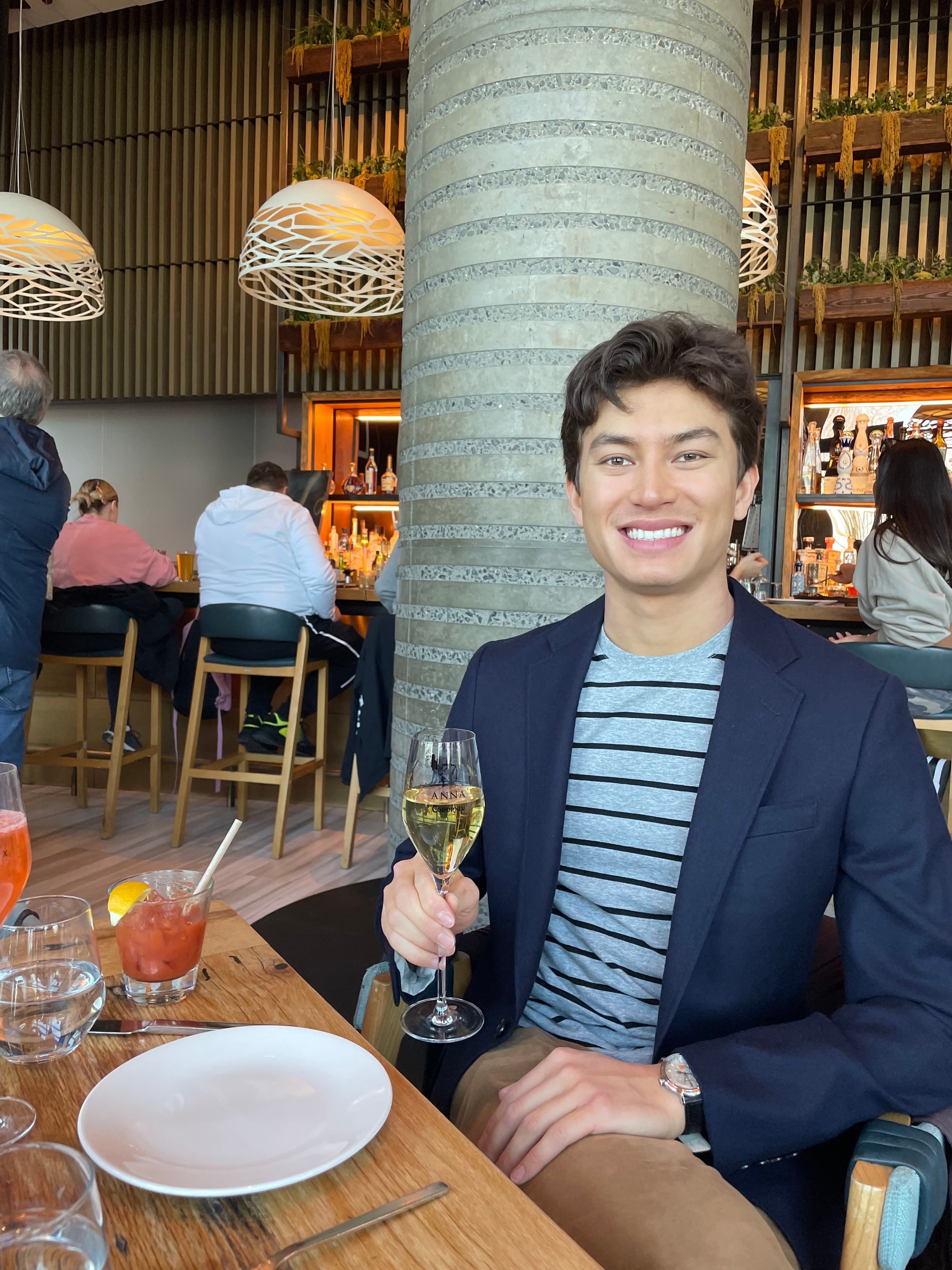 Justin in a striped shirt and blazer holding a glass of wine at a restaurant