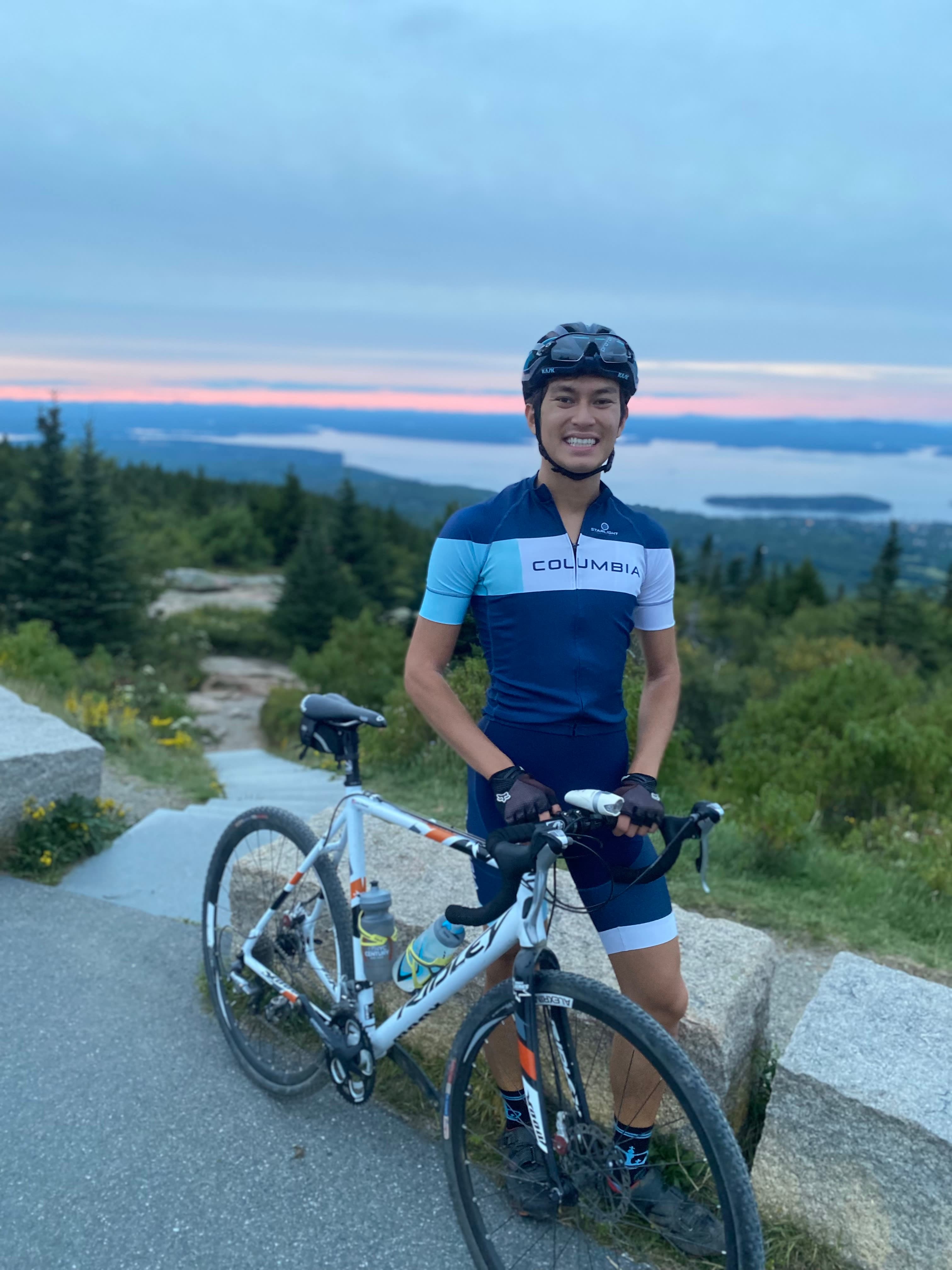 Justin in cycling gear standing next to a bike overlooking trees and a lake