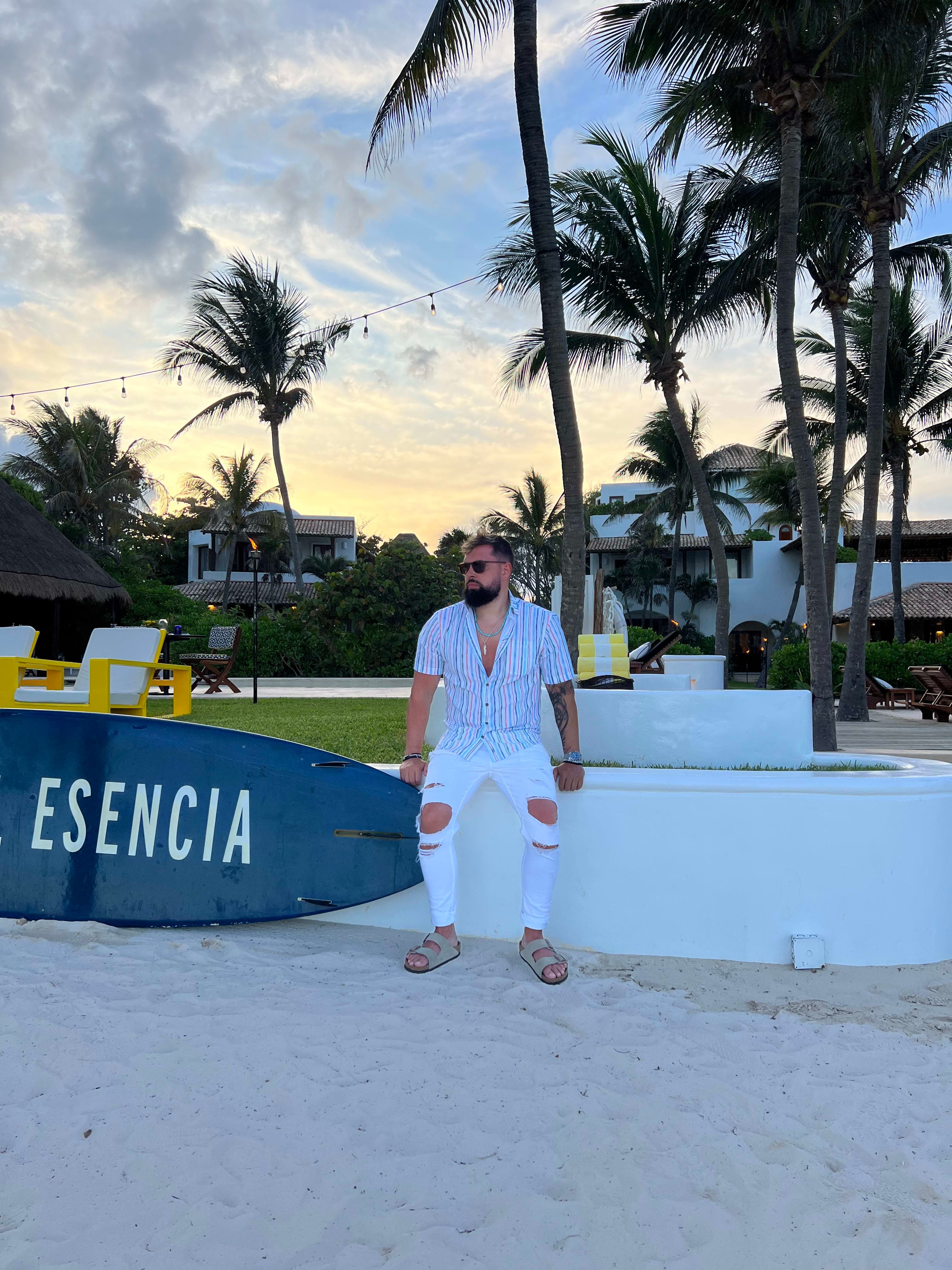 Posing for a photo sitting on a concrete planter with a skate board on the side with Esencia written on it.