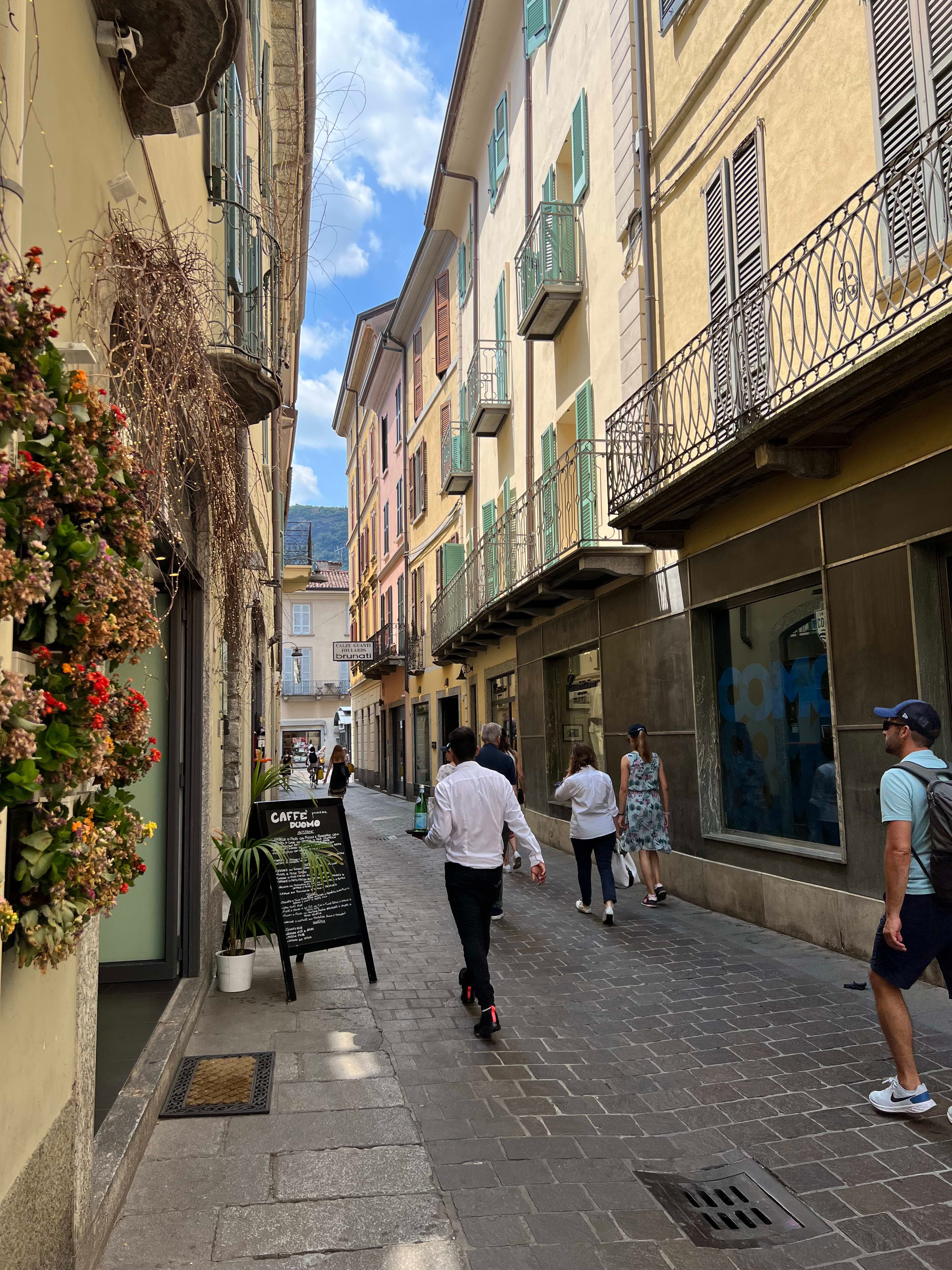 People walking on a narrow street with cafes and shops on both sides