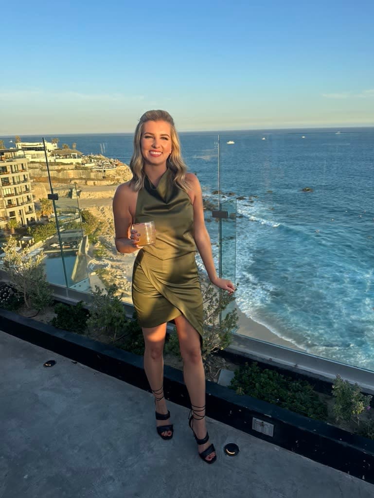 Stefanie posing for a photo standing on a balcony holding a drink in hand with the view of the beach in the background