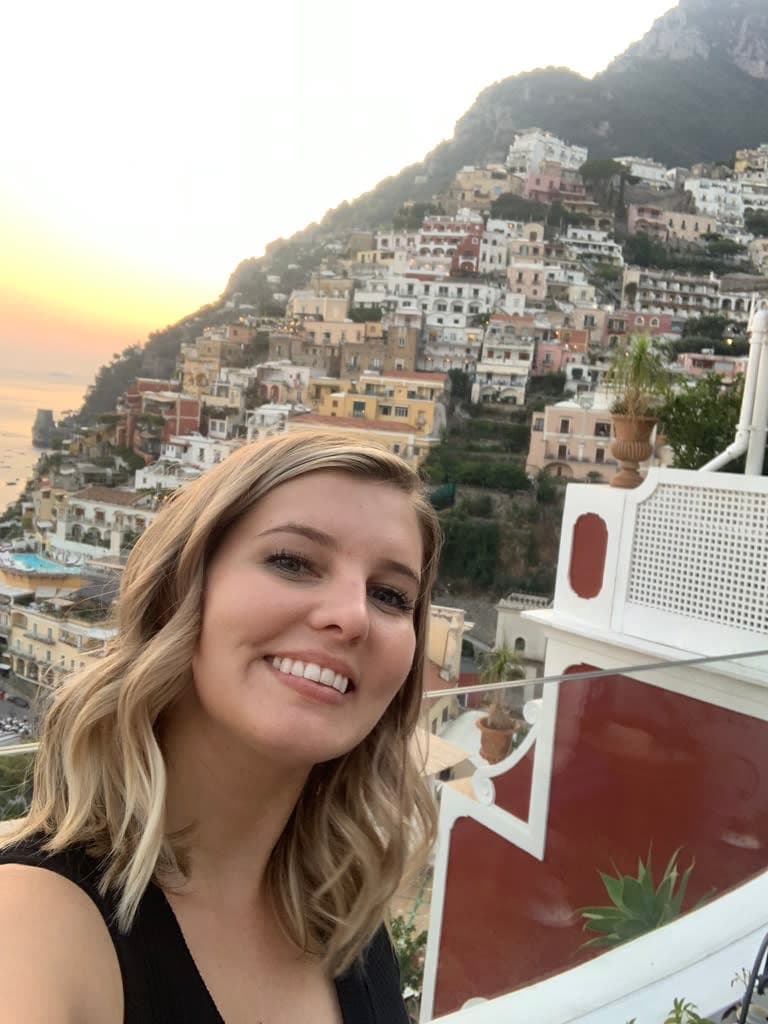 Stefanie standing on a balcony and taking a photo with the town of Positano in view in the background