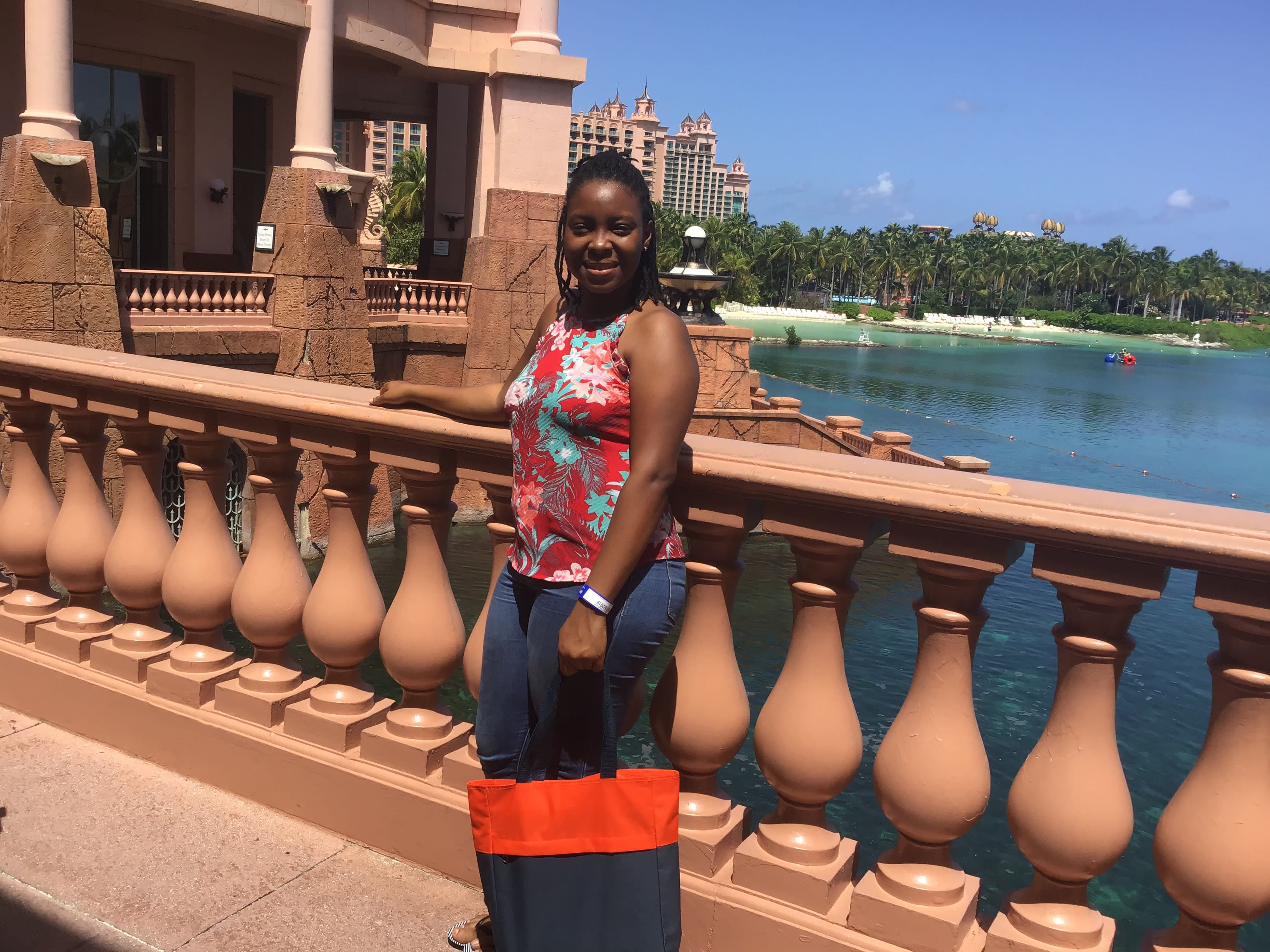 Whitney in a red and white top posing for a photo along a bridge with a beach and resort visible in the background