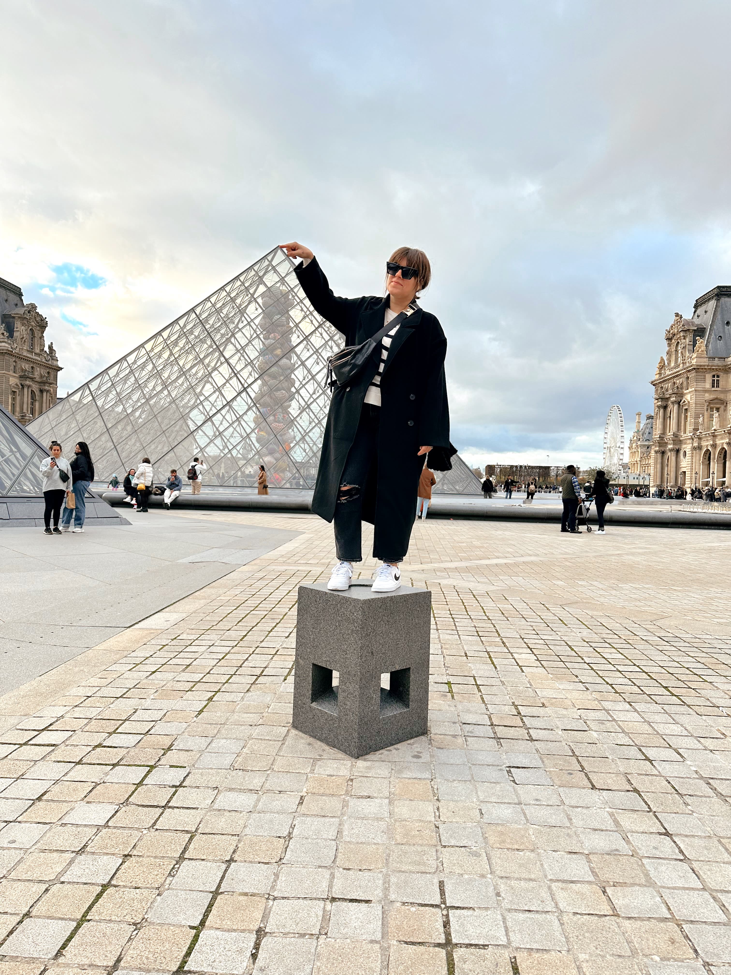 Picture of Leslie posing while placing her finger on the "top" of the Louvre Museum