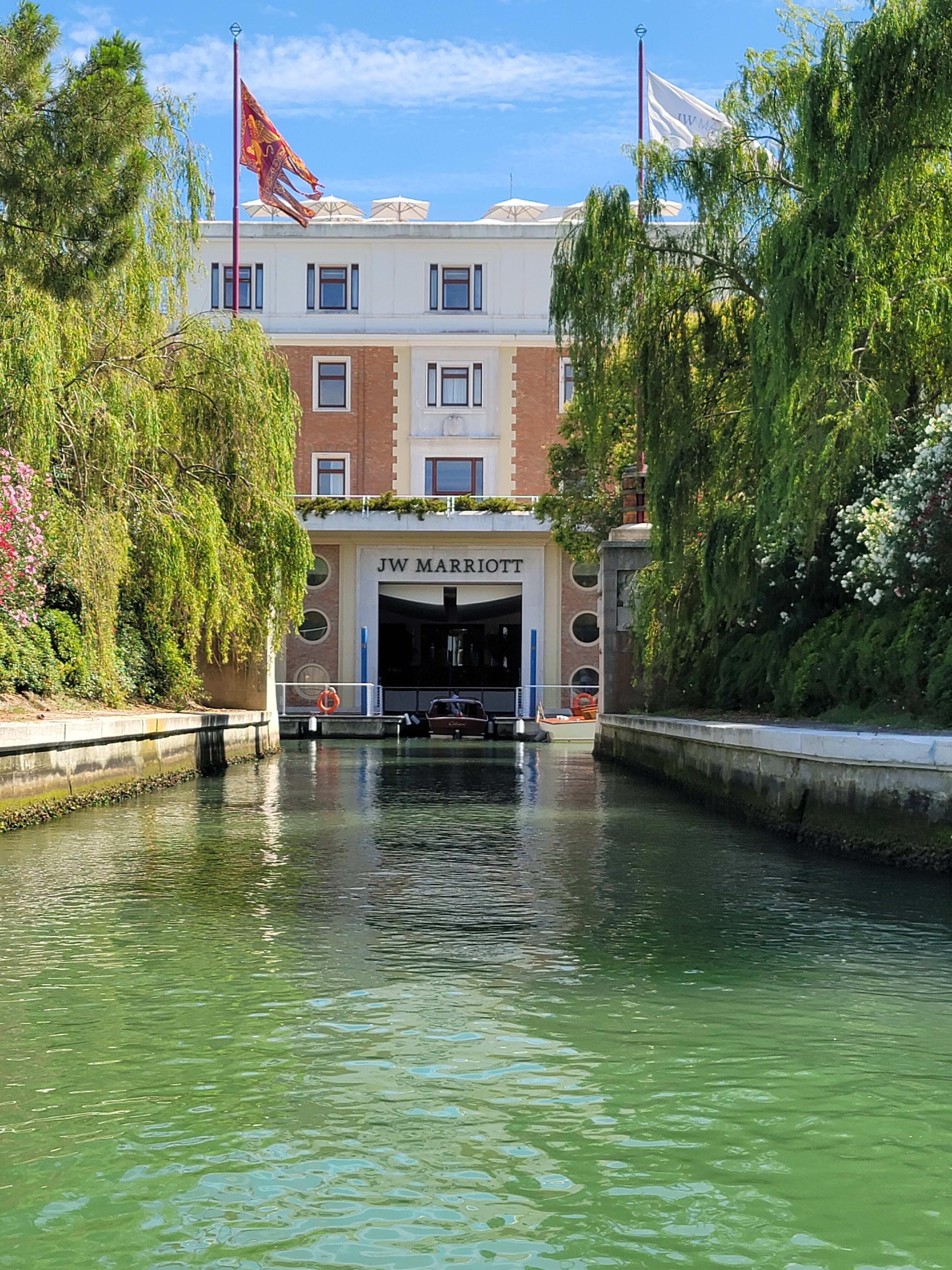 A view of a canal in front of the JW Marriott Venice Resort & Spa with a grand entrance and lush greenery either side