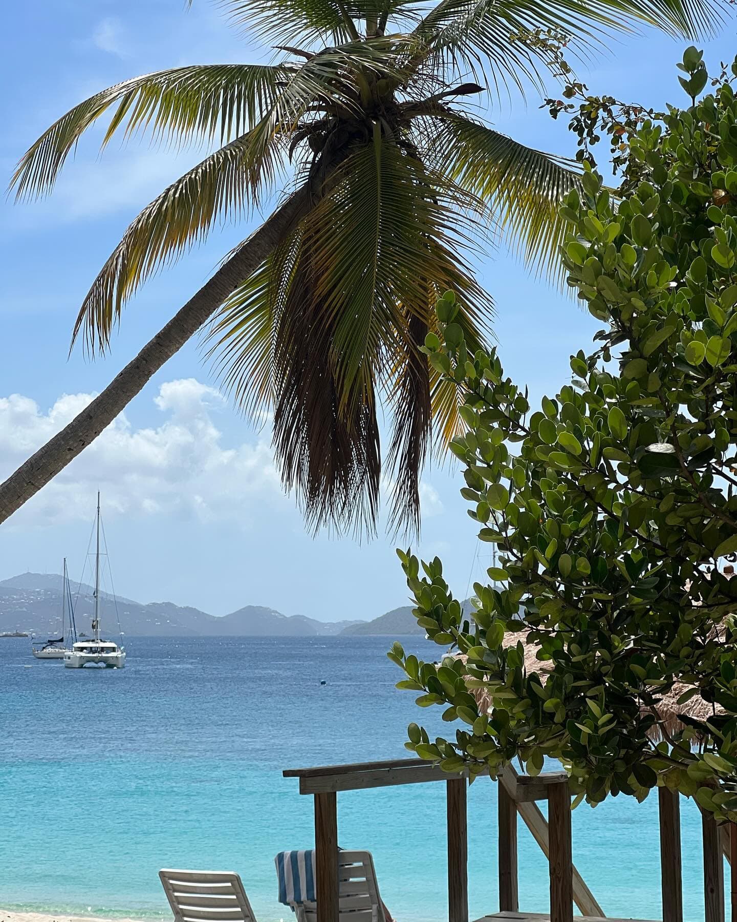 A beach with lounge chairs and palm trees and fishing boats in the sea