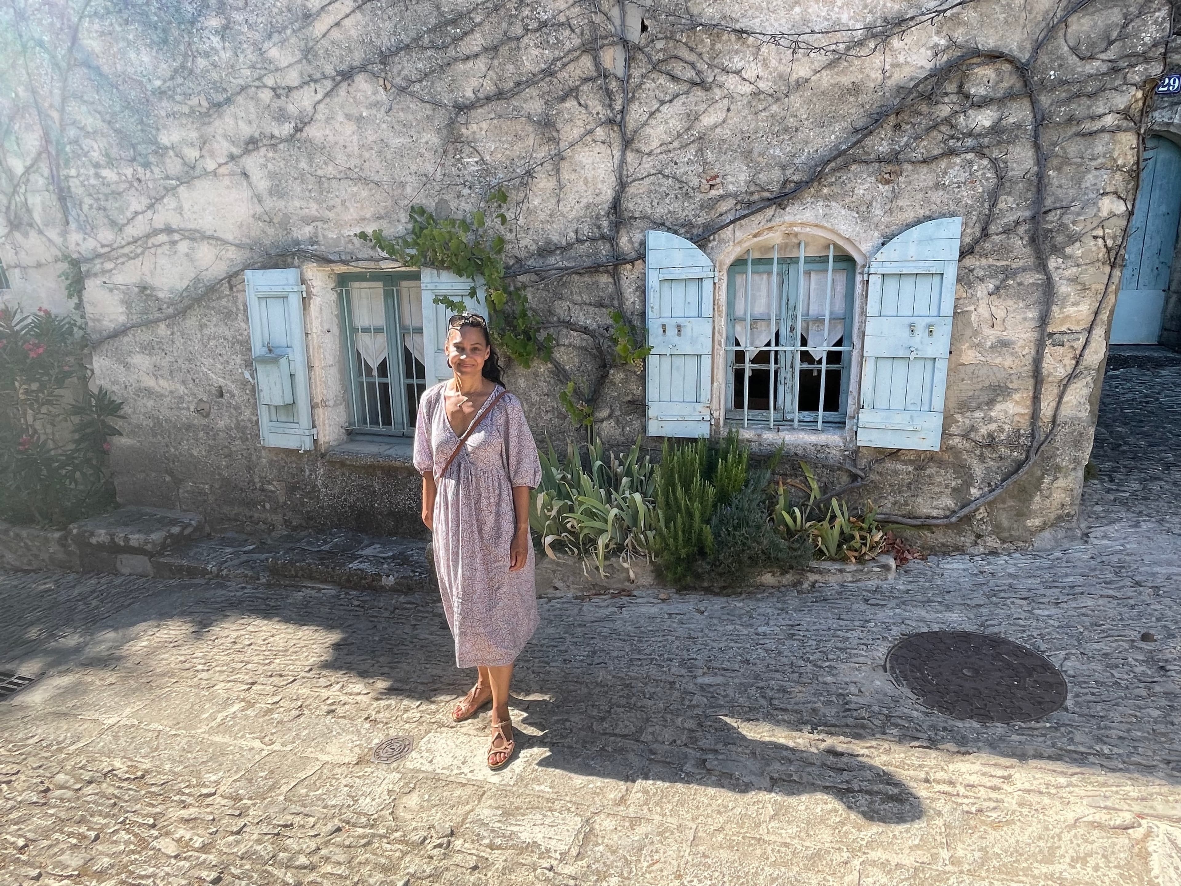 Michaelyn in a purple dress outside a stone house with blue shutters