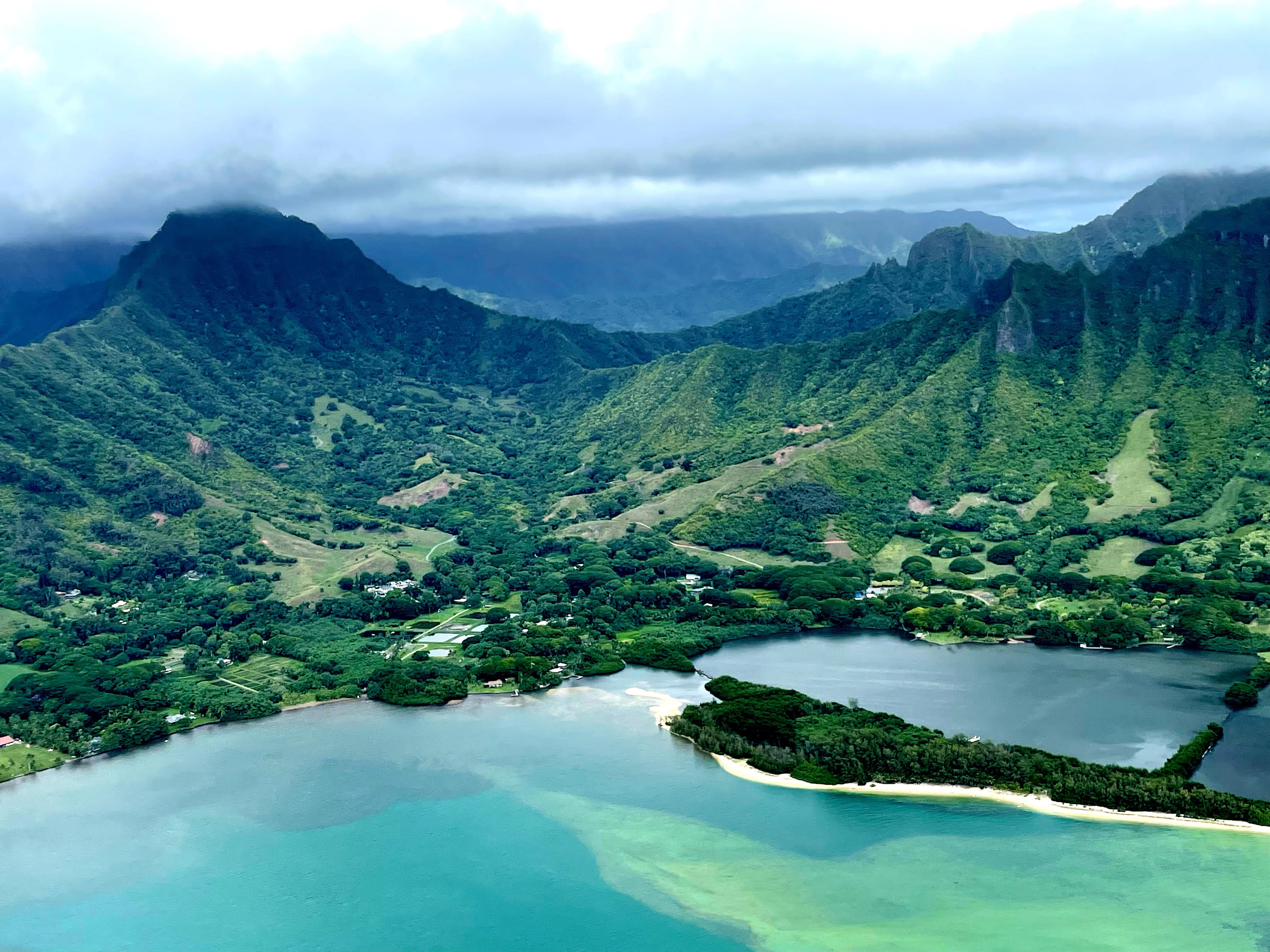Beautiful aerial view of Kualoa with lush green mountains and a body of water with different shades of blue and green