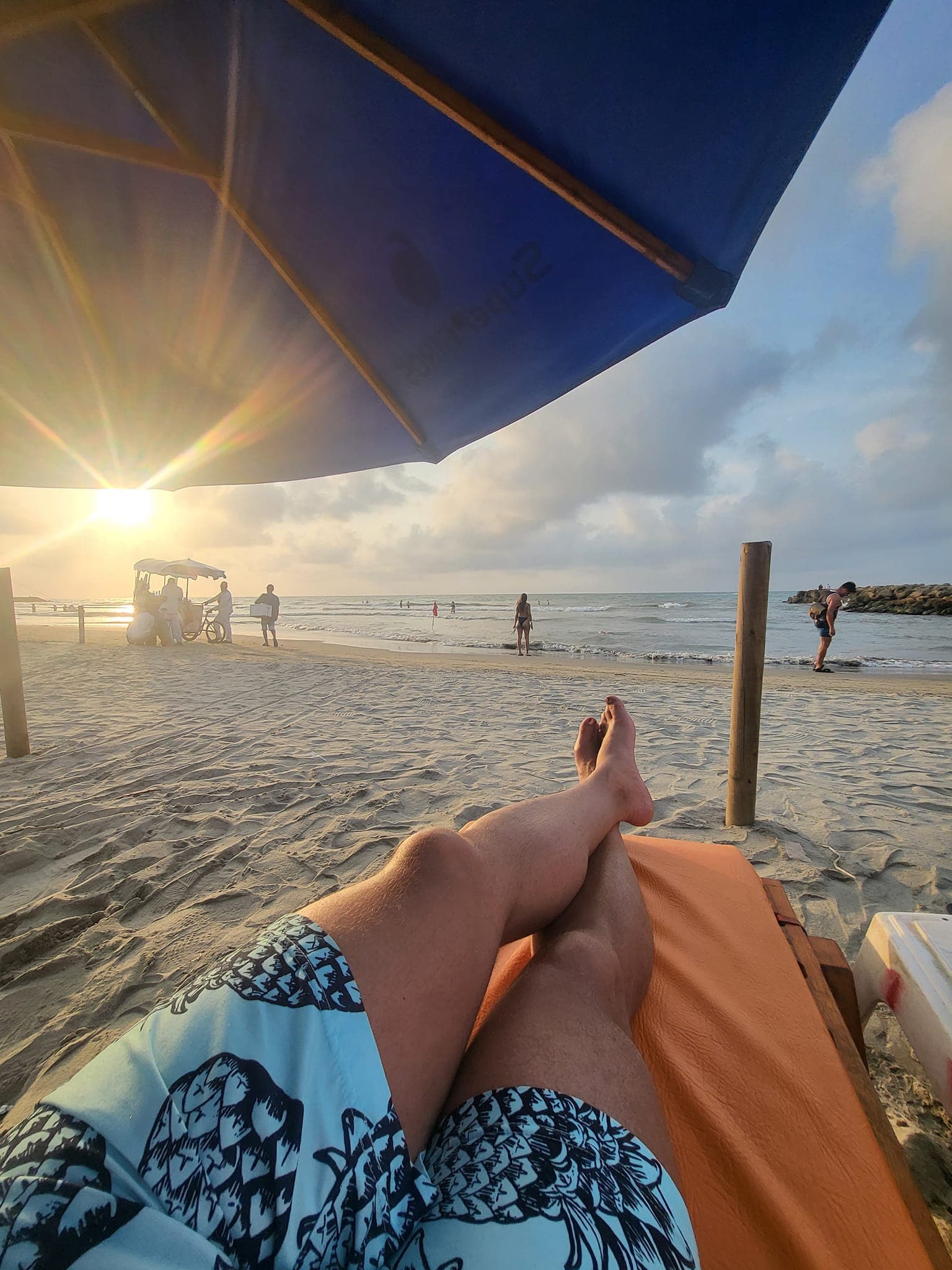 A photo of a man's legs relaxing on a sun lounger on the beach with the sun low in the sky