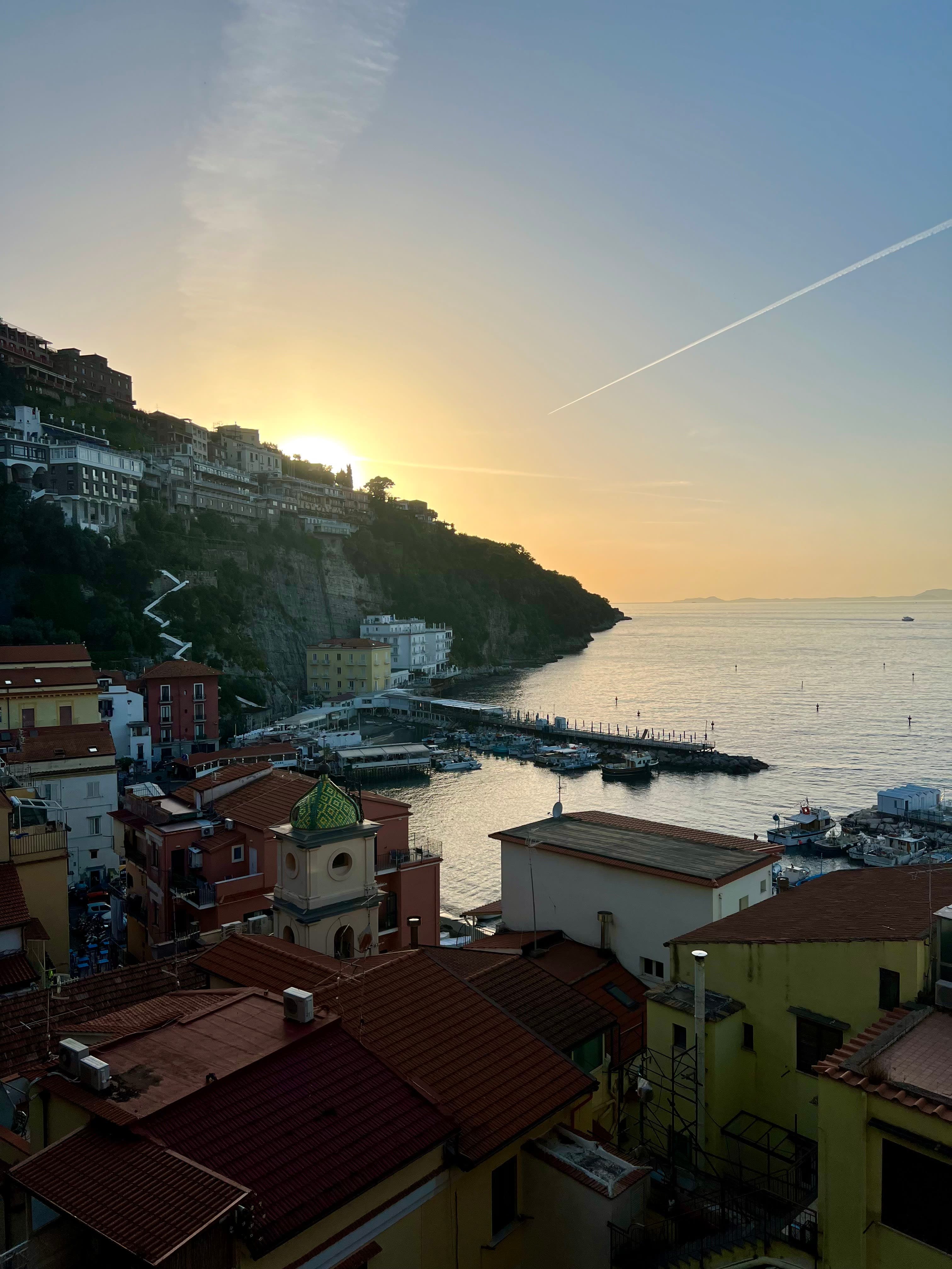 View of the buildings and pier of the Amalfi Coast, with sun setting behind the mountain