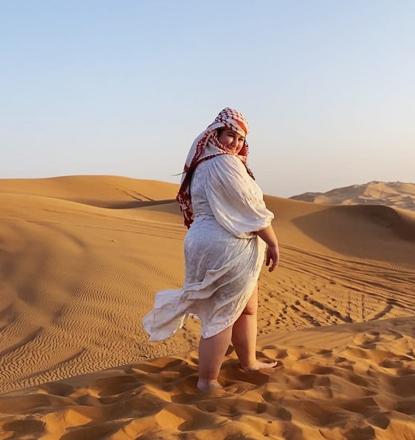 Erika in a white dress and Arabic turban posing for a photo in the desert