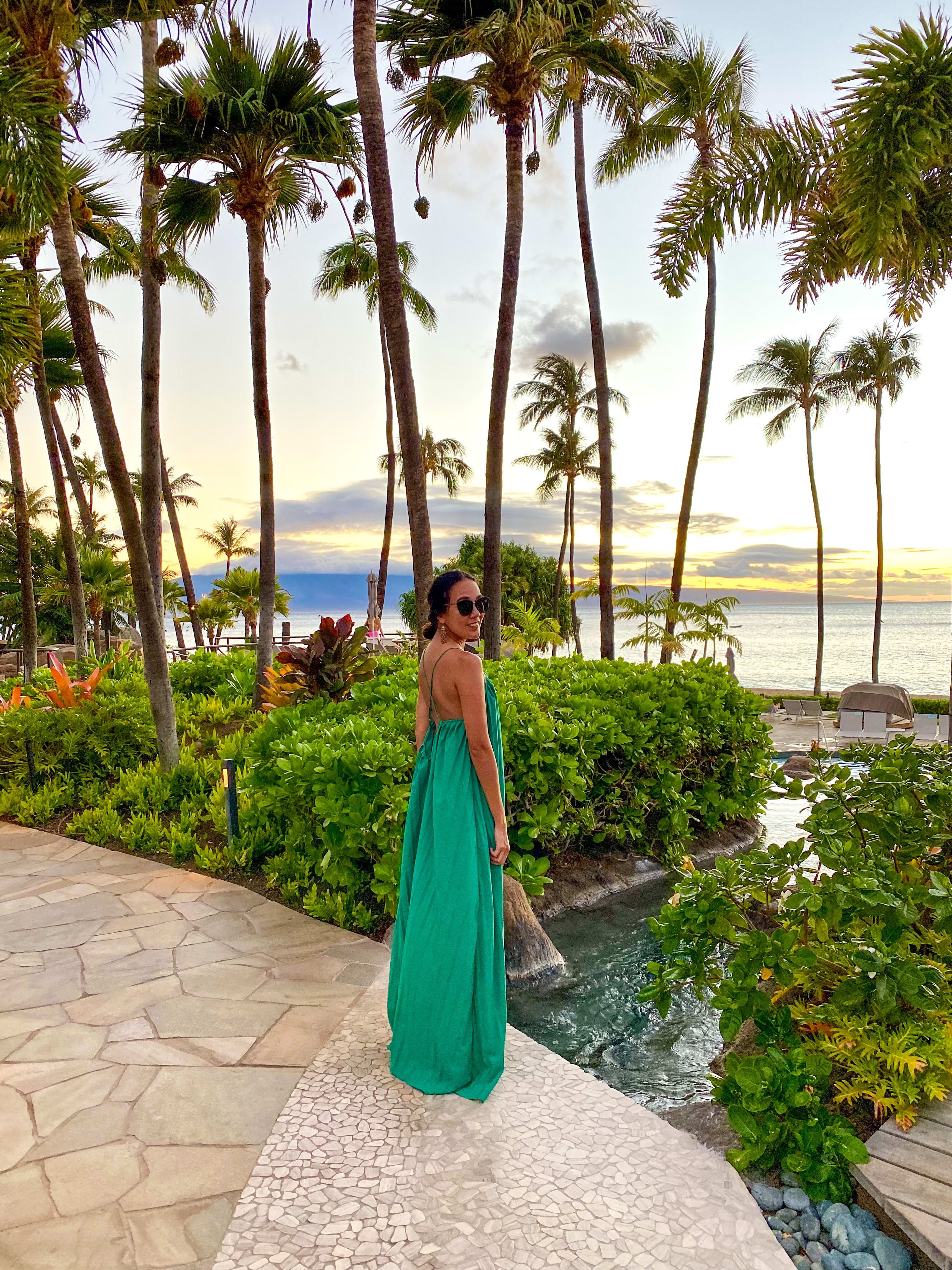 Pam posing for a photo in a green dress, with the beautiful view of palm trees and sea in the background