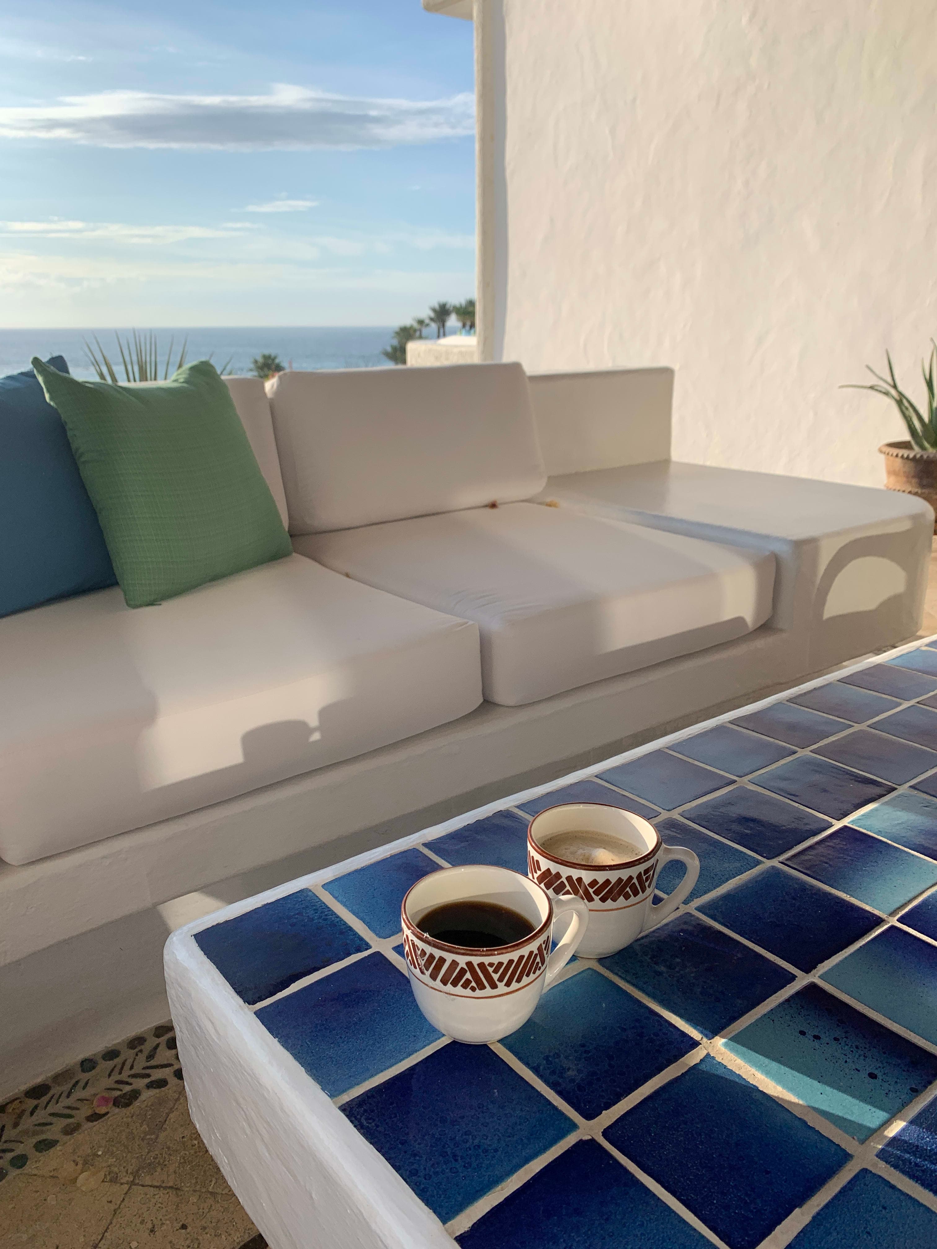 Picture of two coffee cups on a blue tile table with ocean views