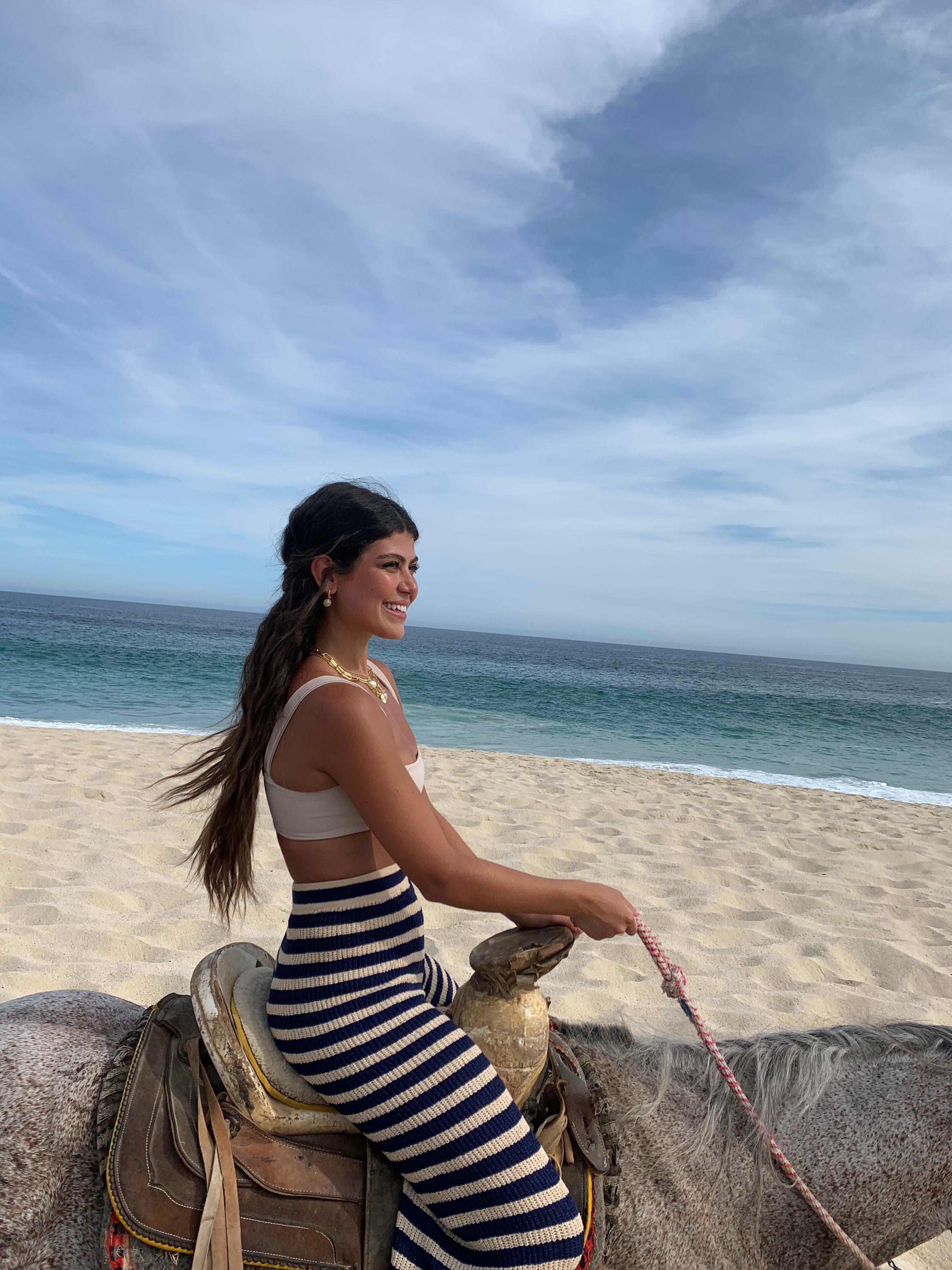Picture of Sophie wearing striped pants riding a horse on the beach