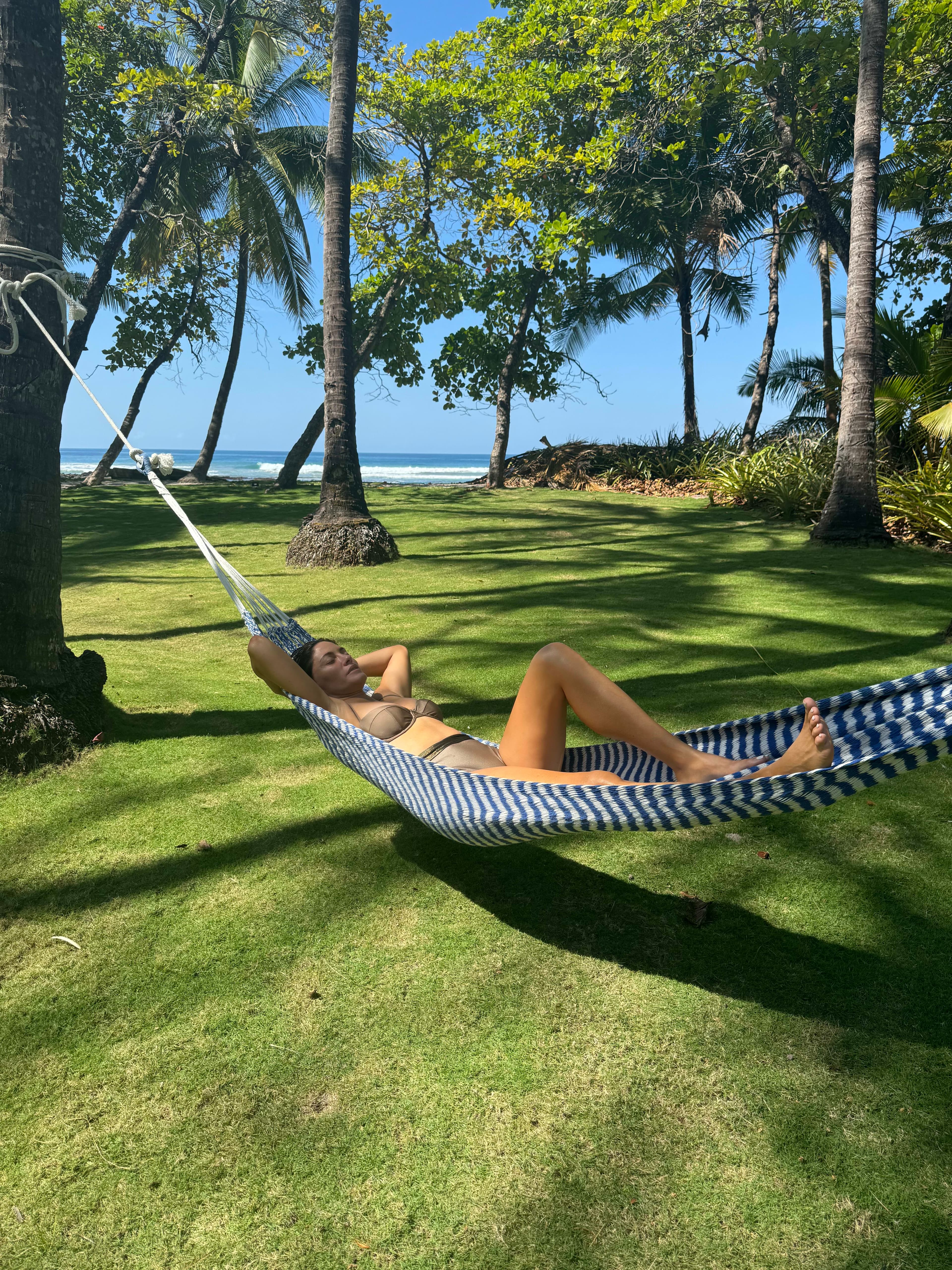 Picture of Shaina in a bathing suit relaxing on a striped hammock surrounded by palm trees