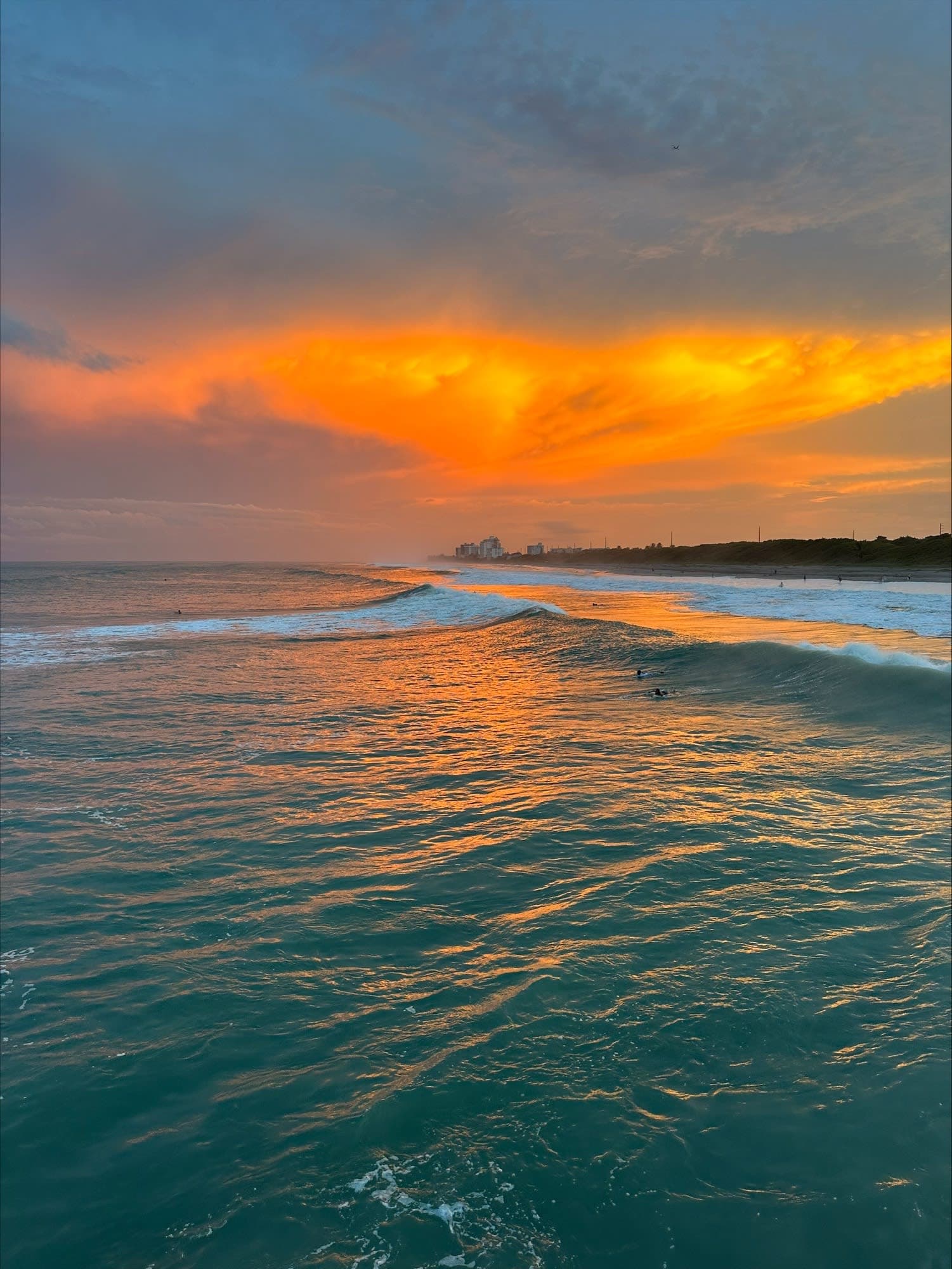 Beautiful orange sunset over the ocean with a wave and surfers in the water
